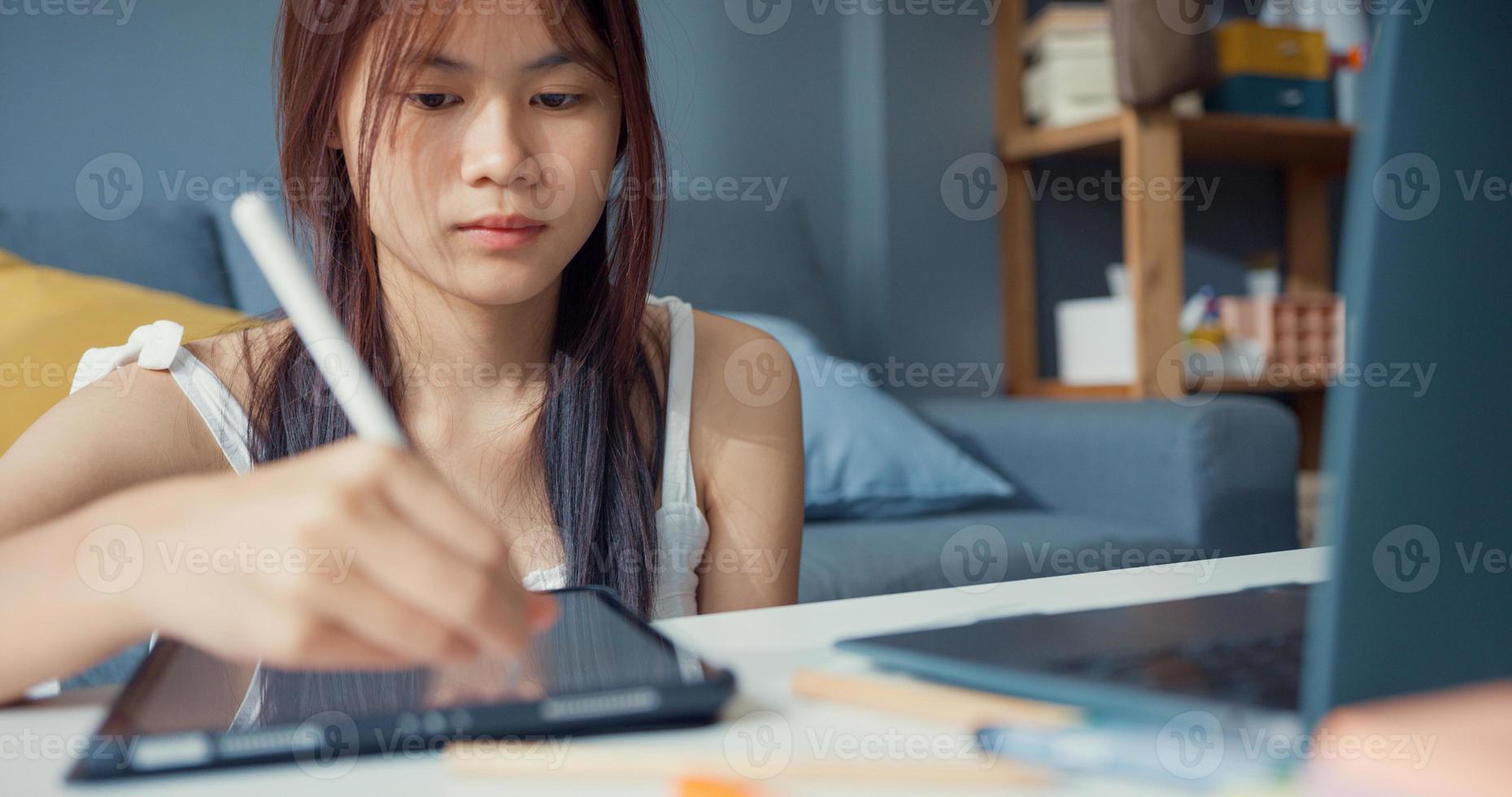 jovem adolescente asiática com foco de laptop de computador de uso casual para aprender palestra de escrita on-line no laptop digital na sala de estar em casa. isolar o conceito de pandemia de coronavírus de e-learning de educação on-line. foto