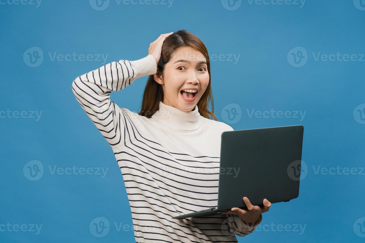 jovem asiática usando laptop com expressão positiva, sorri amplamente, vestida com roupas casuais, sentindo felicidade e carrinho isolado sobre fundo azul. feliz adorável feliz mulher alegra sucesso. foto