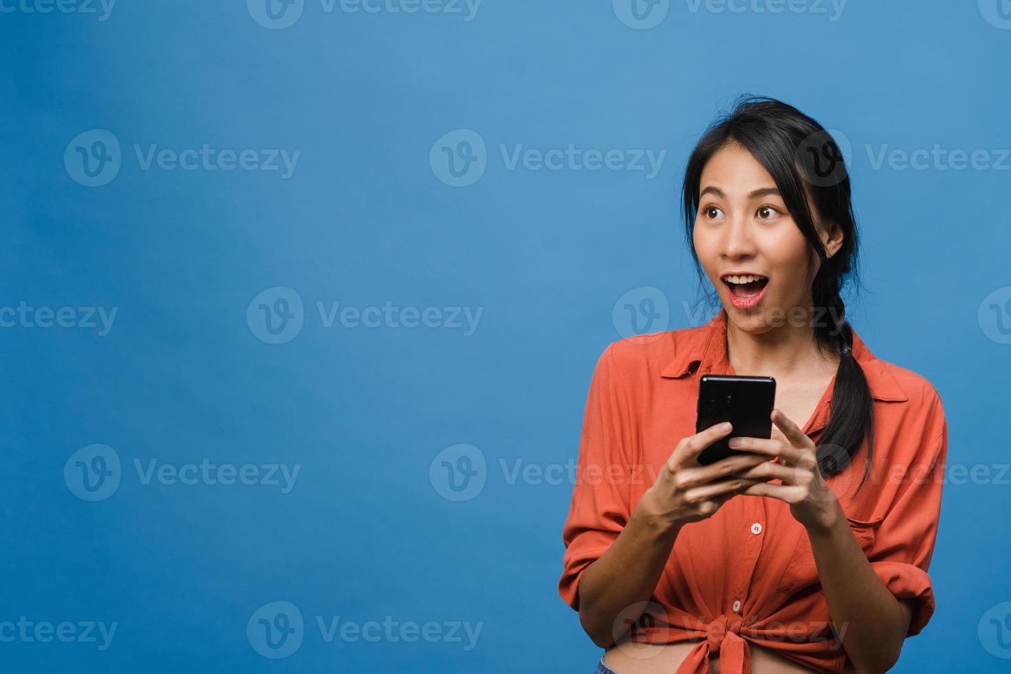 jovem asiática usando telefone com expressão positiva, sorri amplamente, vestida com roupas casuais, sentindo felicidade e carrinho isolado sobre fundo azul. feliz adorável feliz mulher alegra sucesso. foto