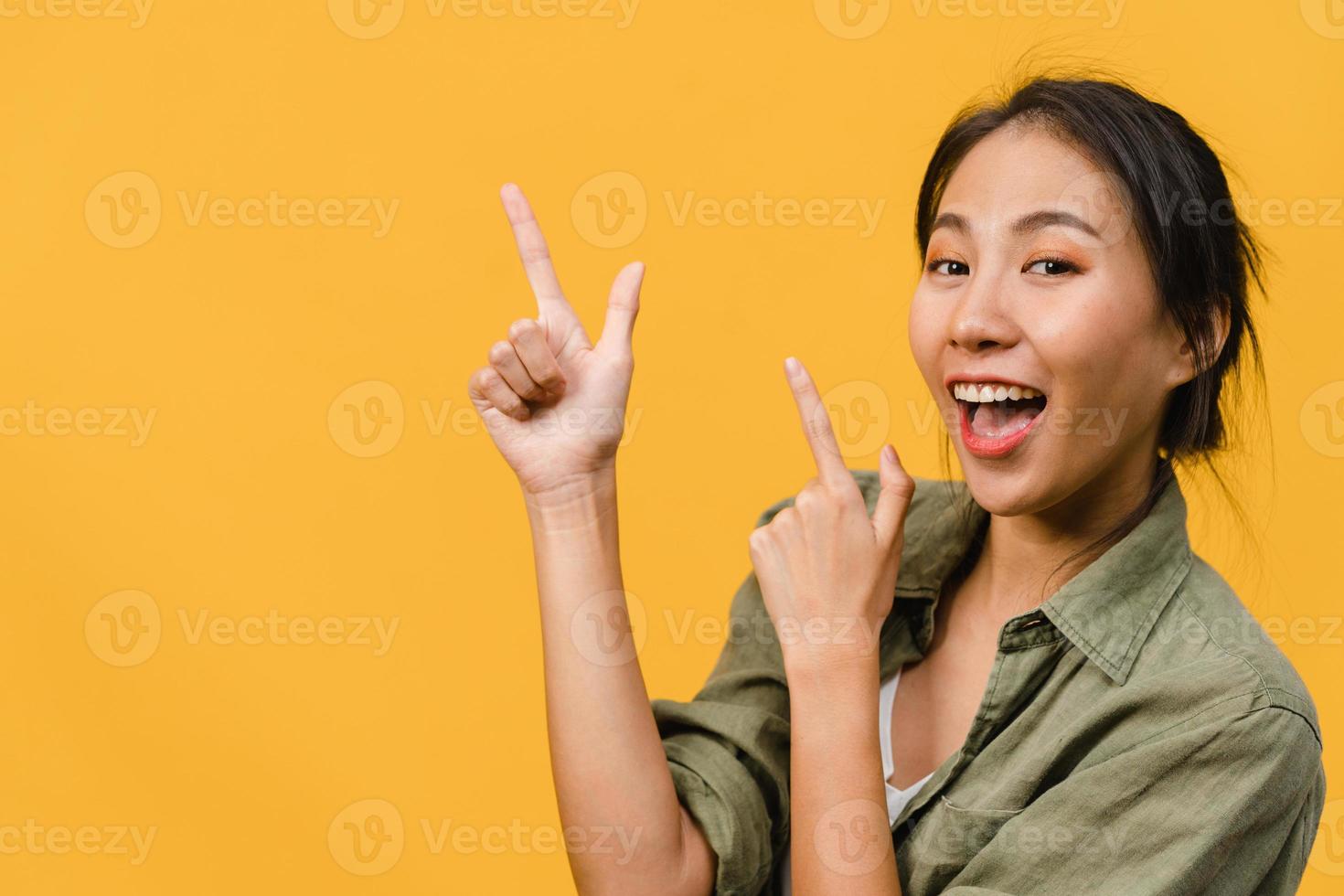 retrato de uma jovem asiática sorrindo com uma expressão alegre, mostra algo incrível no espaço em branco em um pano casual e olhando para a câmera isolada sobre fundo amarelo. conceito de expressão facial. foto