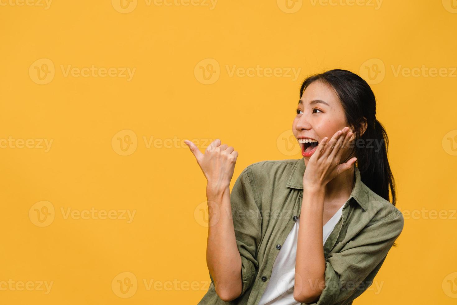 retrato de uma jovem senhora asiática, sorrindo com uma expressão alegre, mostra algo incrível no espaço em branco em roupas casuais e em pé isolado sobre fundo amarelo. conceito de expressão facial. foto