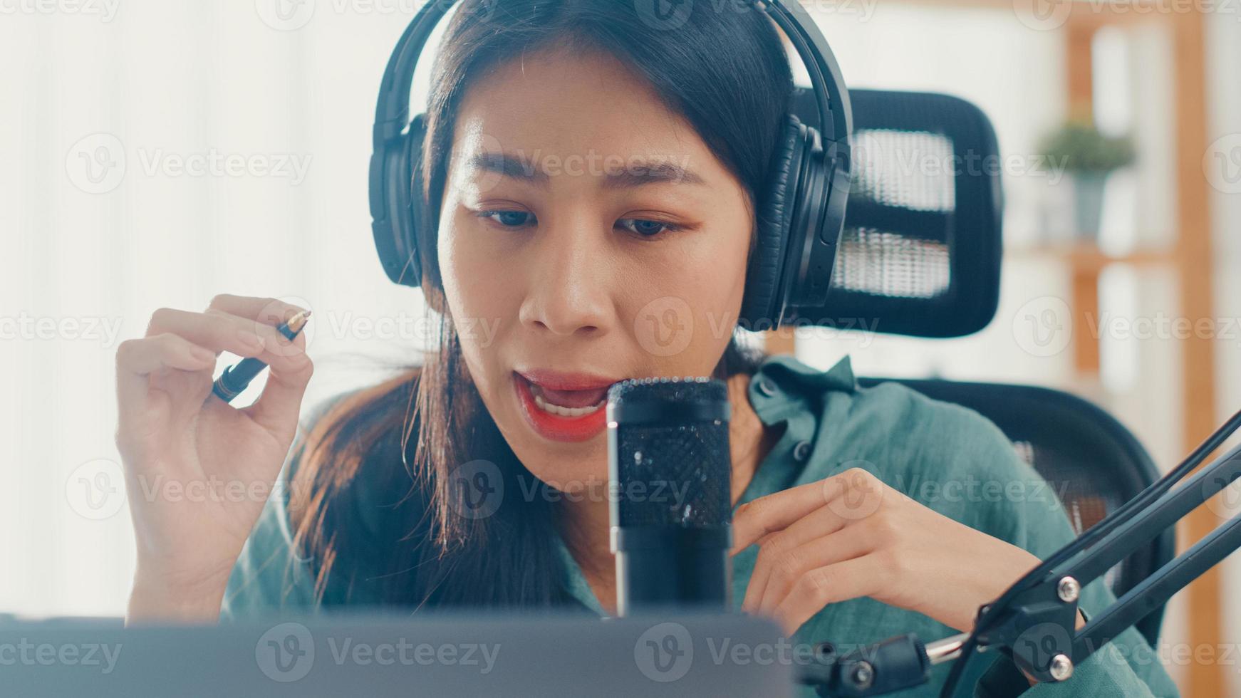 menina asiática feliz gravar um podcast em seu laptop com fones de ouvido e microfone falar com o público em seu quarto. podcaster feminino fazer podcast de áudio de seu estúdio em casa, conceito de ficar em casa. foto