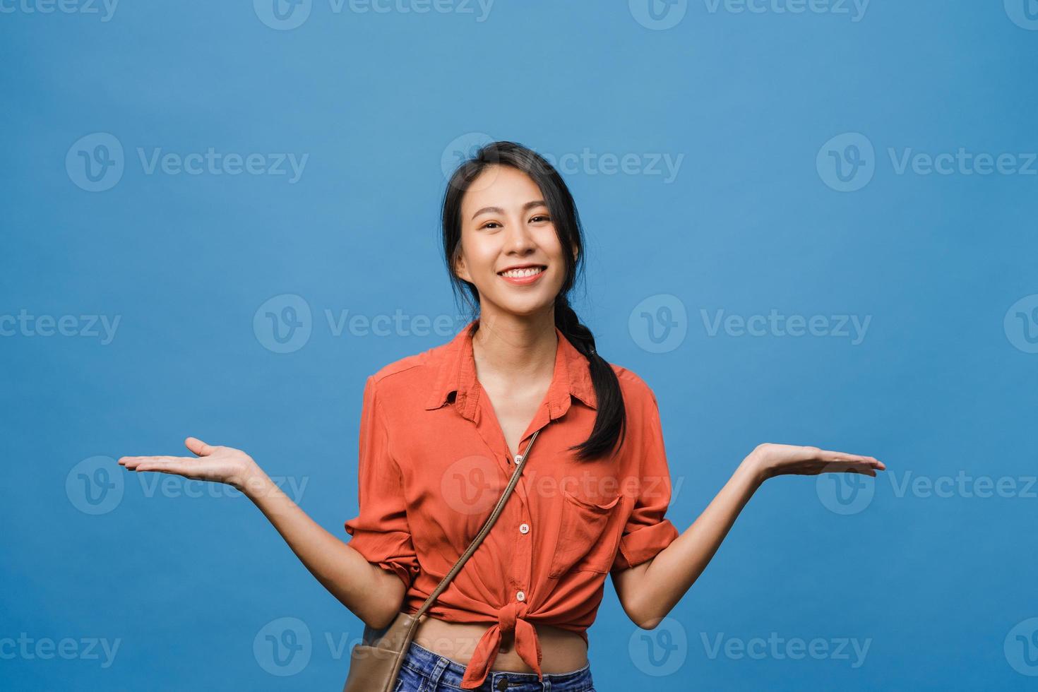 retrato de uma jovem asiática sorrindo com uma expressão alegre, mostra algo incrível no espaço em branco em um pano casual e olhando para a câmera isolada sobre fundo azul. conceito de expressão facial. foto