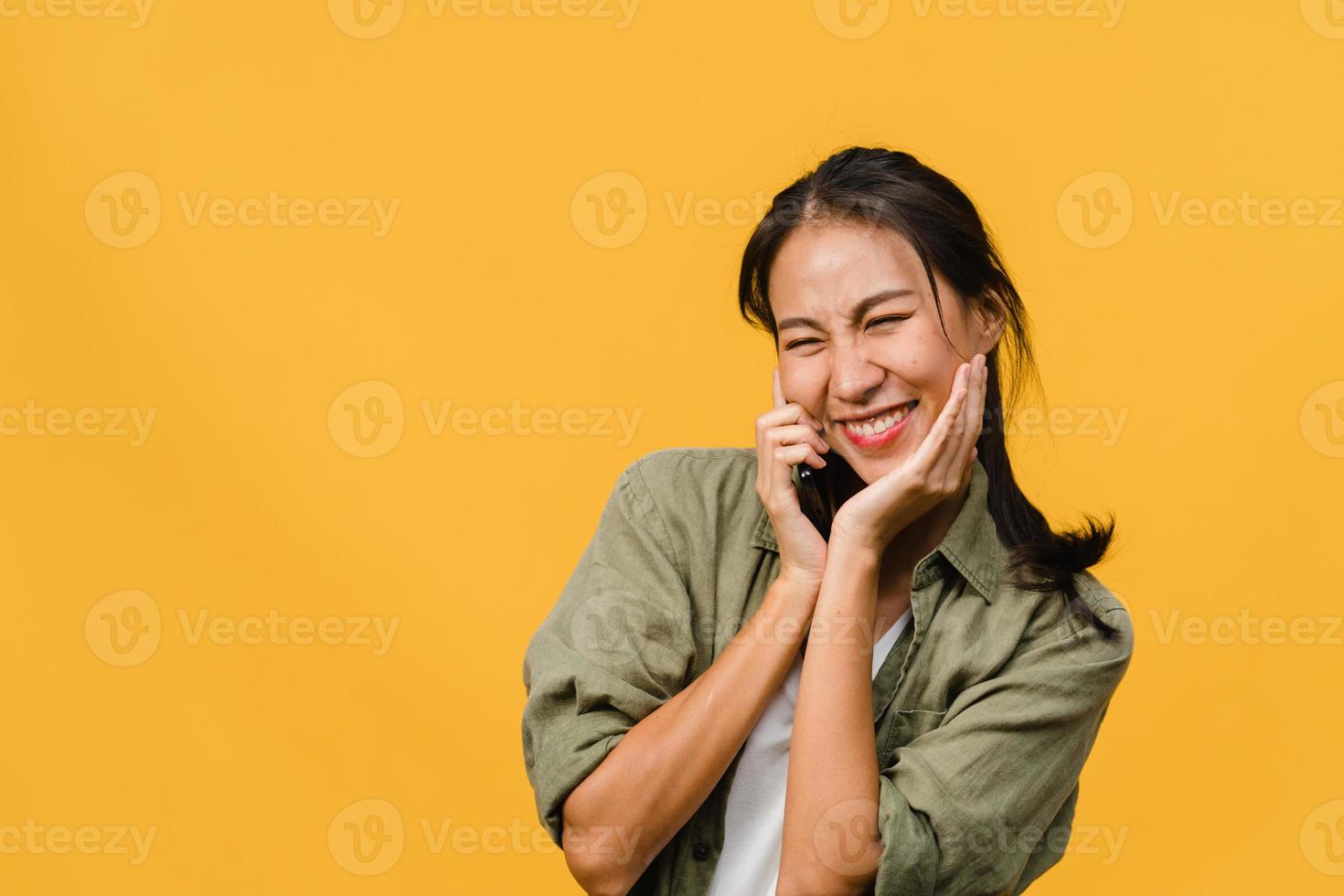 jovem asiática fala por telefone com uma expressão positiva, sorri amplamente, vestida com roupas casuais, sentindo felicidade e fica isolado em um fundo amarelo. feliz adorável feliz mulher alegra sucesso. foto