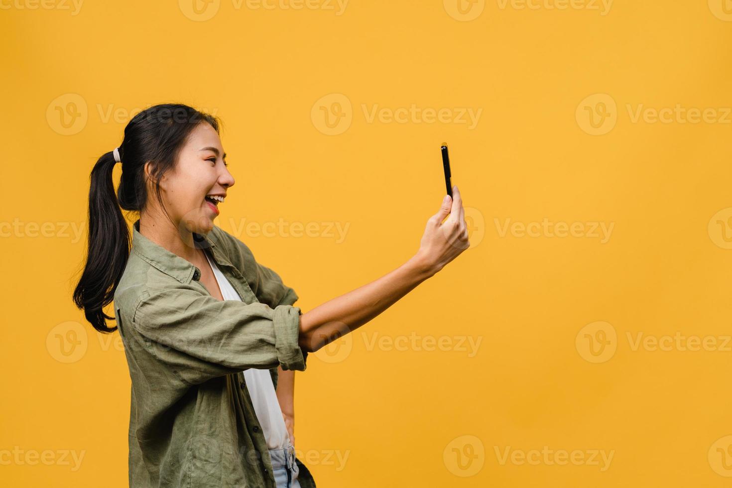 sorrindo adorável mulher asiática fazendo foto de selfie no telefone inteligente com expressão positiva em roupas casuais e ficar isolado em fundo amarelo. feliz adorável feliz mulher alegra sucesso.