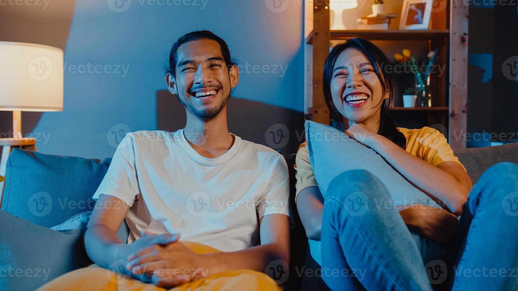 romântico asiático casal homem e mulher sorrir e rir deitar no sofá na sala de estar à noite assistir filme de comédia na televisão juntos em casa. casal casado estilo de vida familiar, conceito de ficar em casa. foto