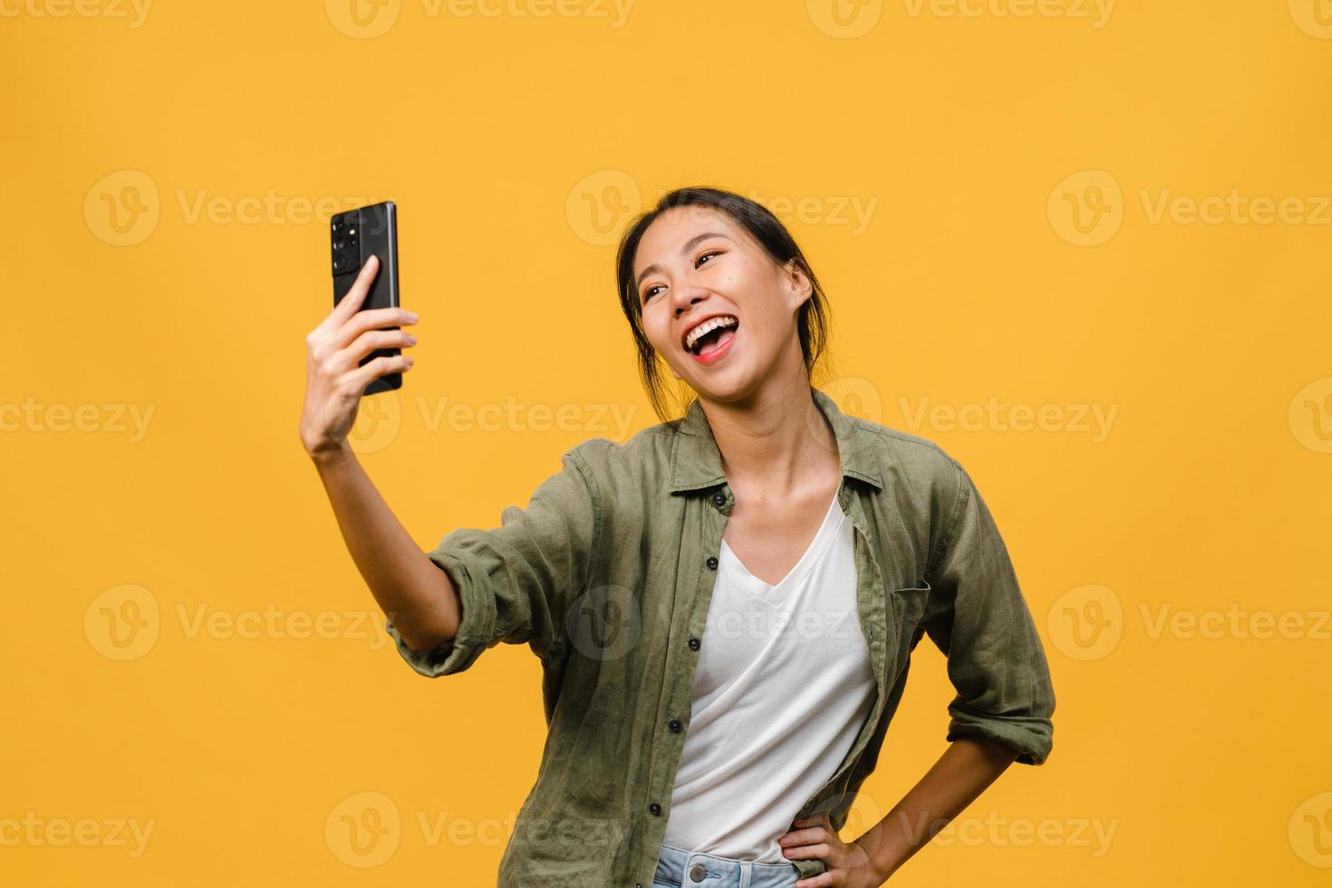 sorrindo adorável mulher asiática fazendo foto de selfie no telefone inteligente com expressão positiva em roupas casuais e ficar isolado em fundo amarelo. feliz adorável feliz mulher alegra sucesso.