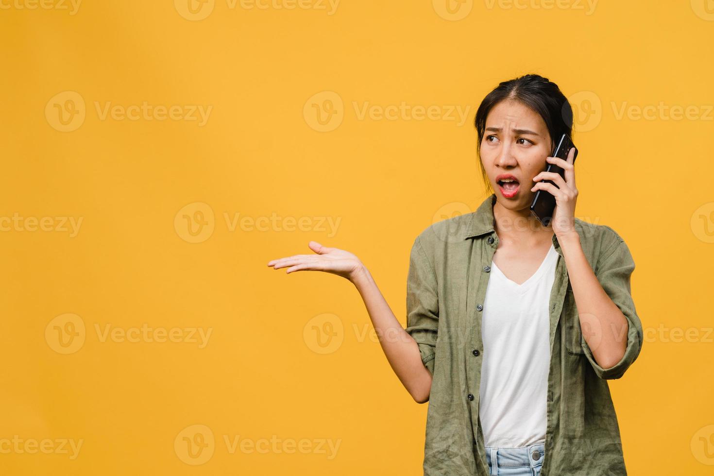 jovem asiática fala por telefone com expressão negativa, gritando animado, chora com raiva emocional em um pano casual e fica isolado em um fundo amarelo com espaço de cópia em branco. conceito de expressão facial. foto