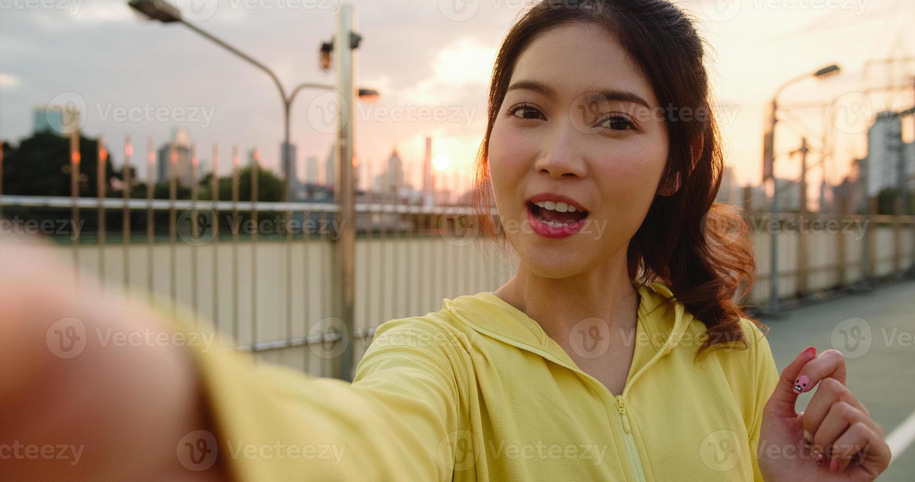 atraente jovem atleta da ásia influenciador senhora gravando vídeo vlog ao vivo no upload do telefone nas redes sociais enquanto se exercita na cidade urbana. desportista vestindo roupas esportivas na rua pela manhã. foto