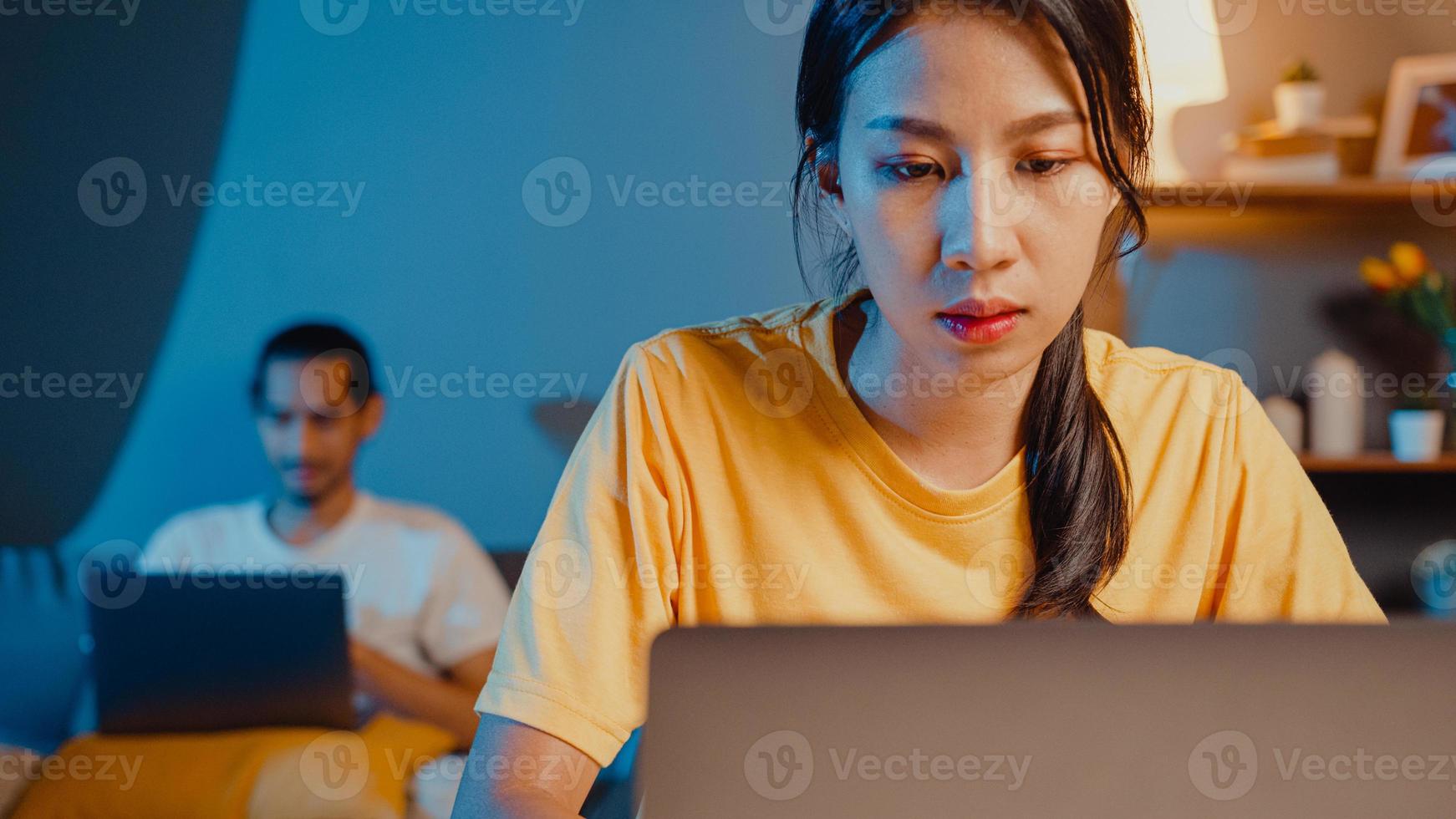 casal asiático freelance homem e mulher casuais esposa foco negócio de trabalho financeiro no computador portátil na mesa à noite videochamada do marido feliz com o resto da família deitou-se depois do trabalho no sofá em casa. foto