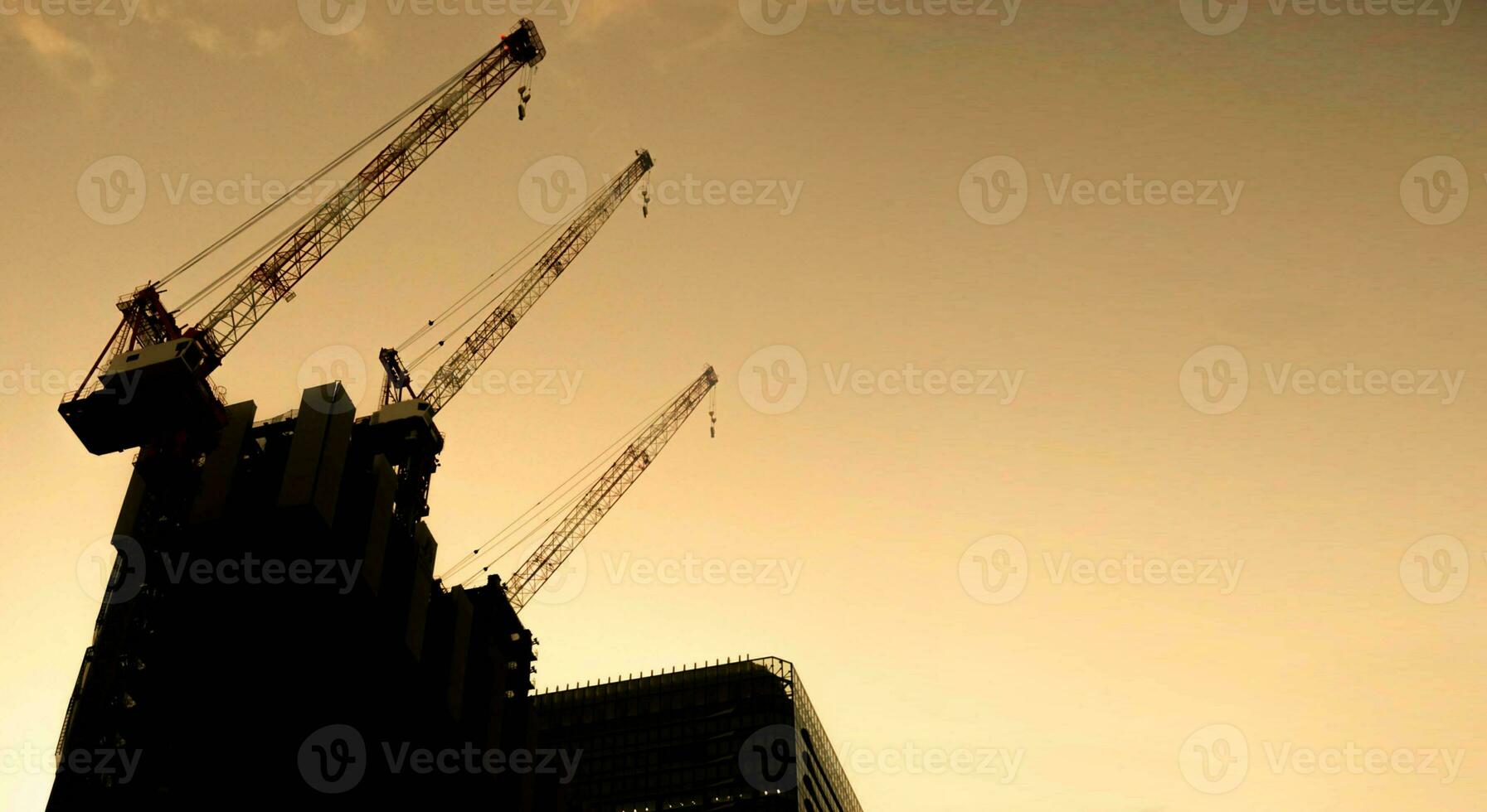 borrado e silhueta elevação guindastes máquina para mover materiais às construção construção local em pôr do sol céu fundo foto