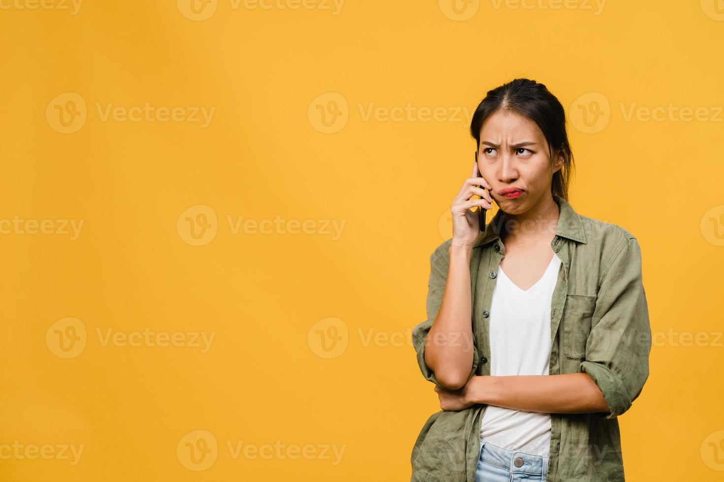 jovem asiática fala por telefone com expressão negativa, gritando animado, chora com raiva emocional em um pano casual e fica isolado em um fundo amarelo com espaço de cópia em branco. conceito de expressão facial. foto