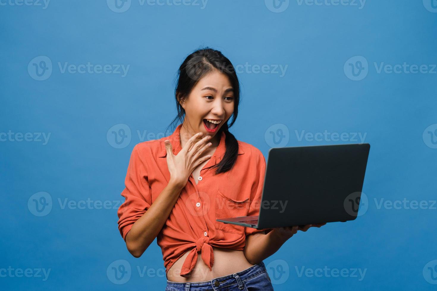 jovem asiática usando laptop com expressão positiva, sorri amplamente, vestida com roupas casuais, sentindo felicidade e carrinho isolado sobre fundo azul. feliz adorável feliz mulher alegra sucesso. foto