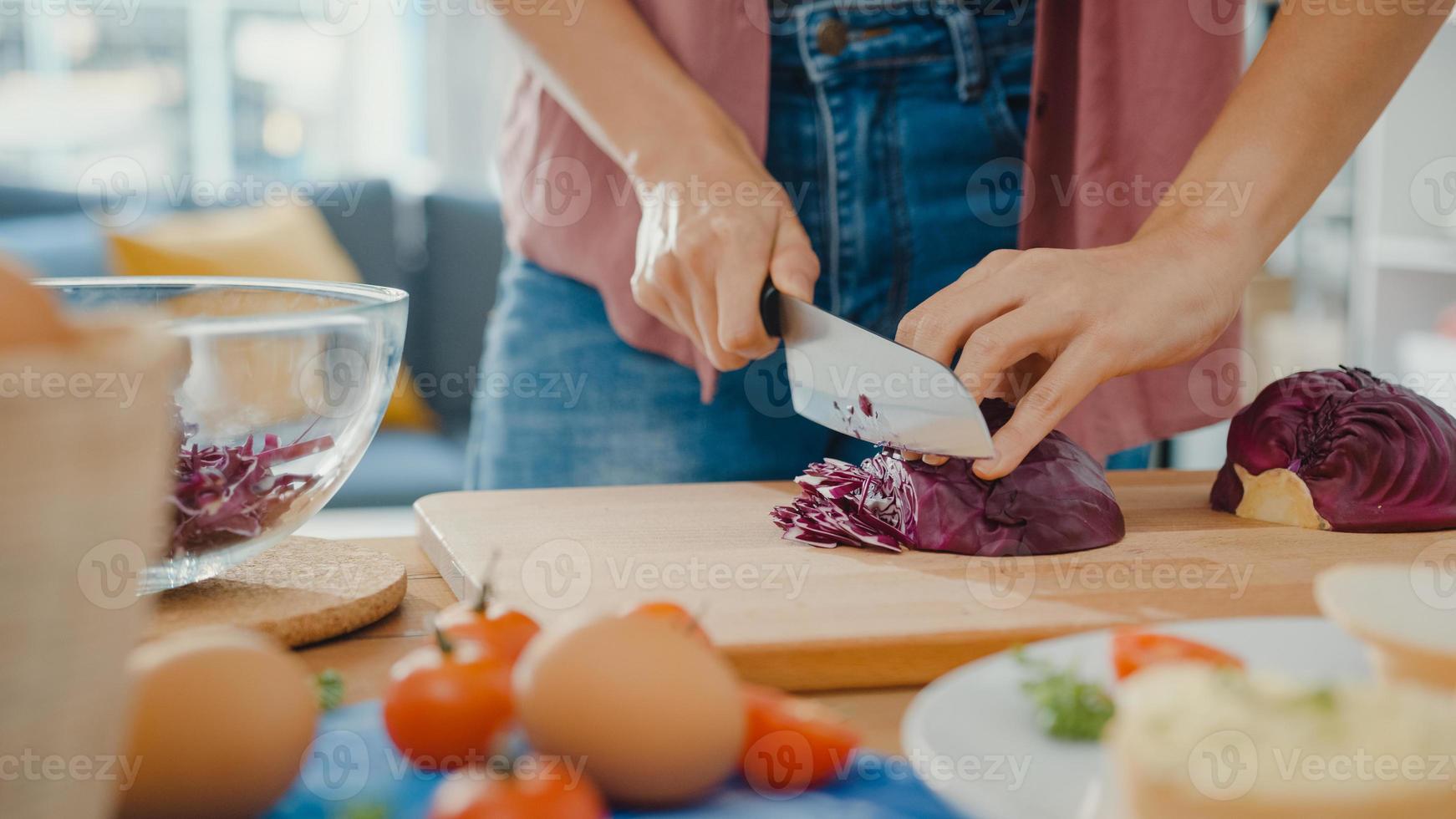 mão do chef jovem mulher asiática segurar faca corte repolho chinês vermelho na placa de madeira na mesa da cozinha em casa. cozinhar salada de legumes, comer alimentos saudáveis de estilo de vida e o conceito natural tradicional. foto