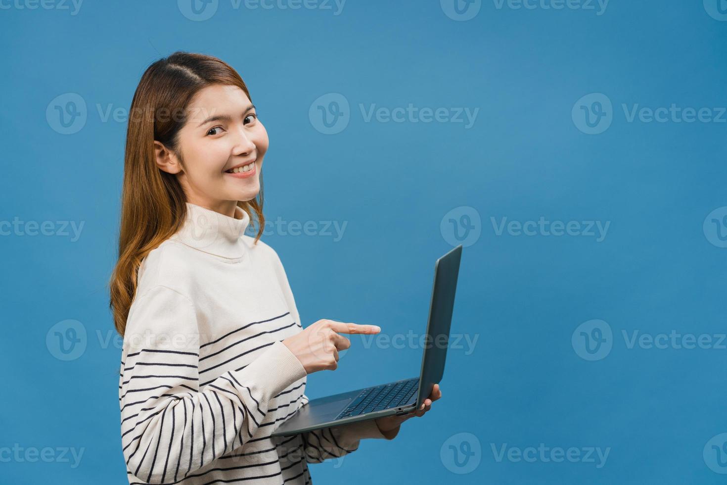 jovem asiática usando laptop com expressão positiva, sorri amplamente, vestida com roupas casuais, sentindo felicidade e carrinho isolado sobre fundo azul. feliz adorável feliz mulher alegra sucesso. foto