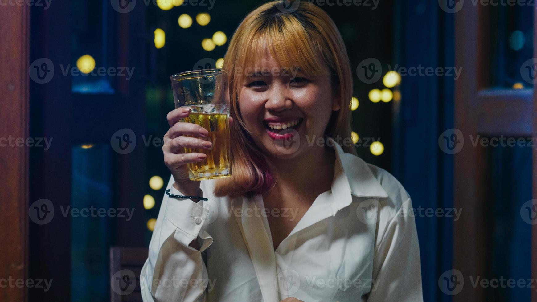 jovem asiática bebendo cerveja se divertindo feliz noite festa ano novo evento on-line celebração via videochamada por telefone em casa à noite. distância social, quarentena para coronavírus. ponto de vista ou pov foto