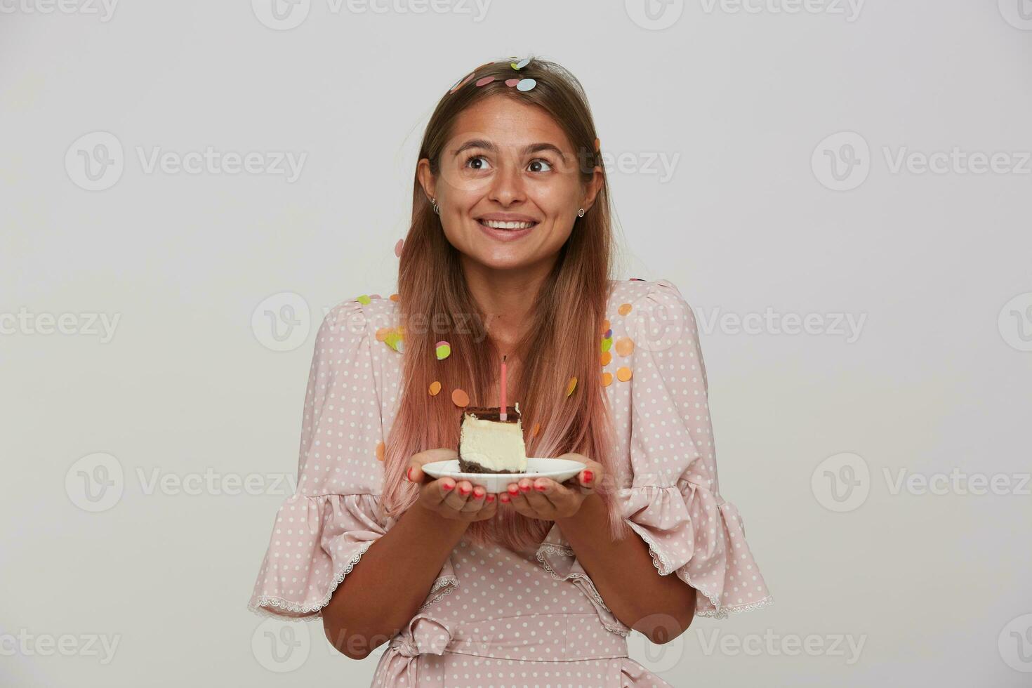 retrato do Boa olhando positivo jovem grandes cabelos senhora dentro festivo roupas a comemorar dela aniversário e em pé sobre branco fundo com peça do bolo dentro elevado mãos foto