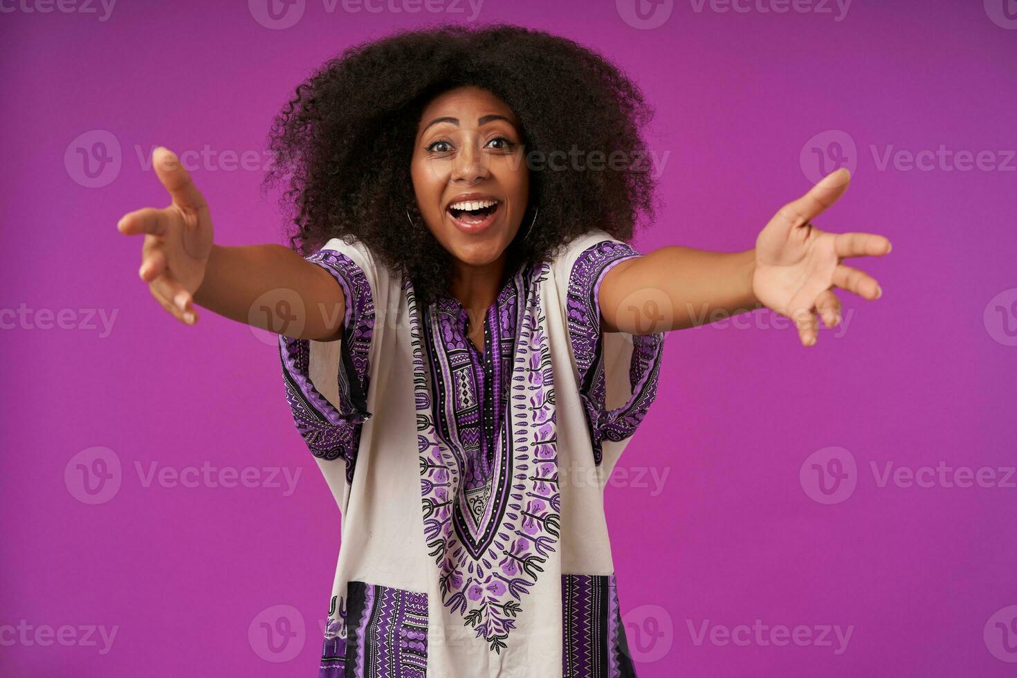 muito feliz jovem bonita Sombrio esfolado fêmea com casual Penteado vestindo branco estampado camisa, posando sobre roxa fundo com aberto braços e indo para dar abraço foto