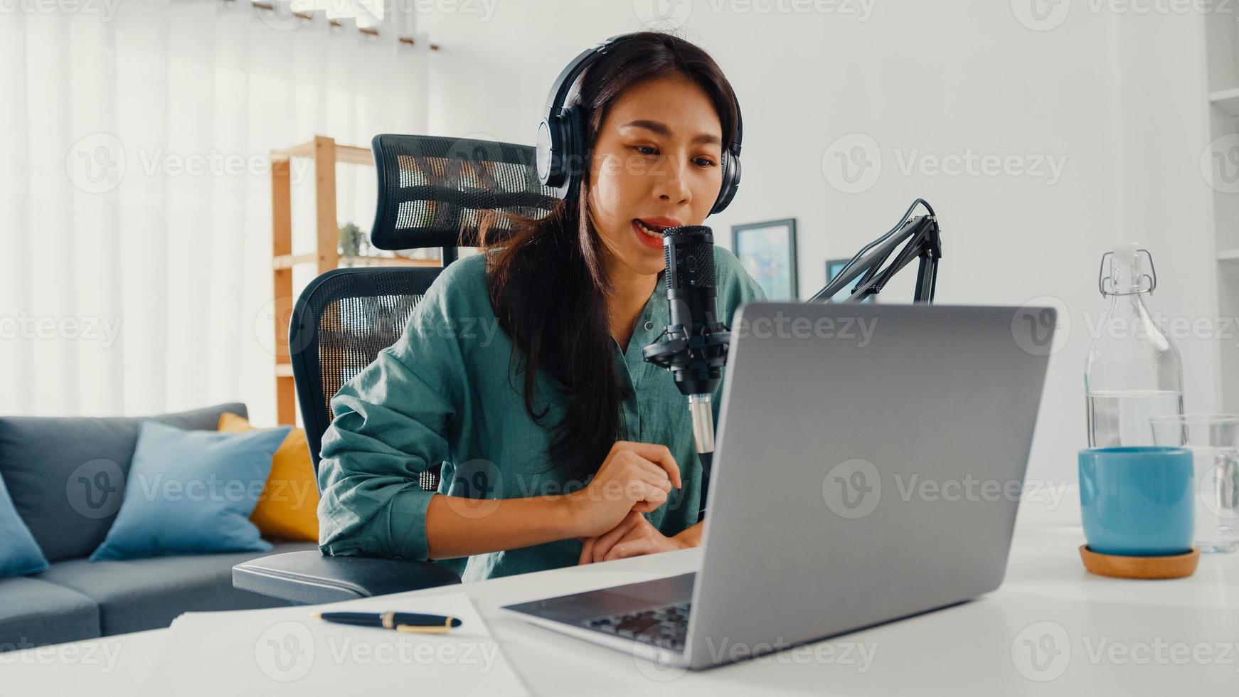 menina asiática feliz gravar um podcast em seu laptop com fones de ouvido e microfone falar com o público em seu quarto. podcaster feminino fazer podcast de áudio de seu estúdio em casa, conceito de ficar em casa. foto