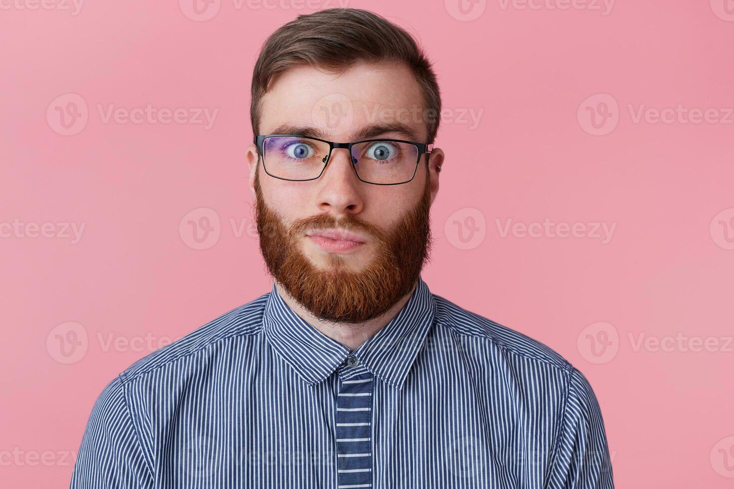 fechar acima retrato do engraçado gengibre cara dentro óculos e listrado camisa olhando às Câmera, isolado em Rosa fundo foto