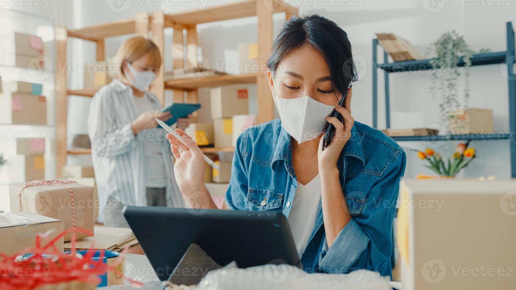 jovens empresárias asiáticas usam máscara facial usando telefone celular para receber pedidos de compra e verificar produtos em estoque, trabalham no escritório doméstico. proprietário de uma pequena empresa, conceito freelance de entrega de mercado online. foto