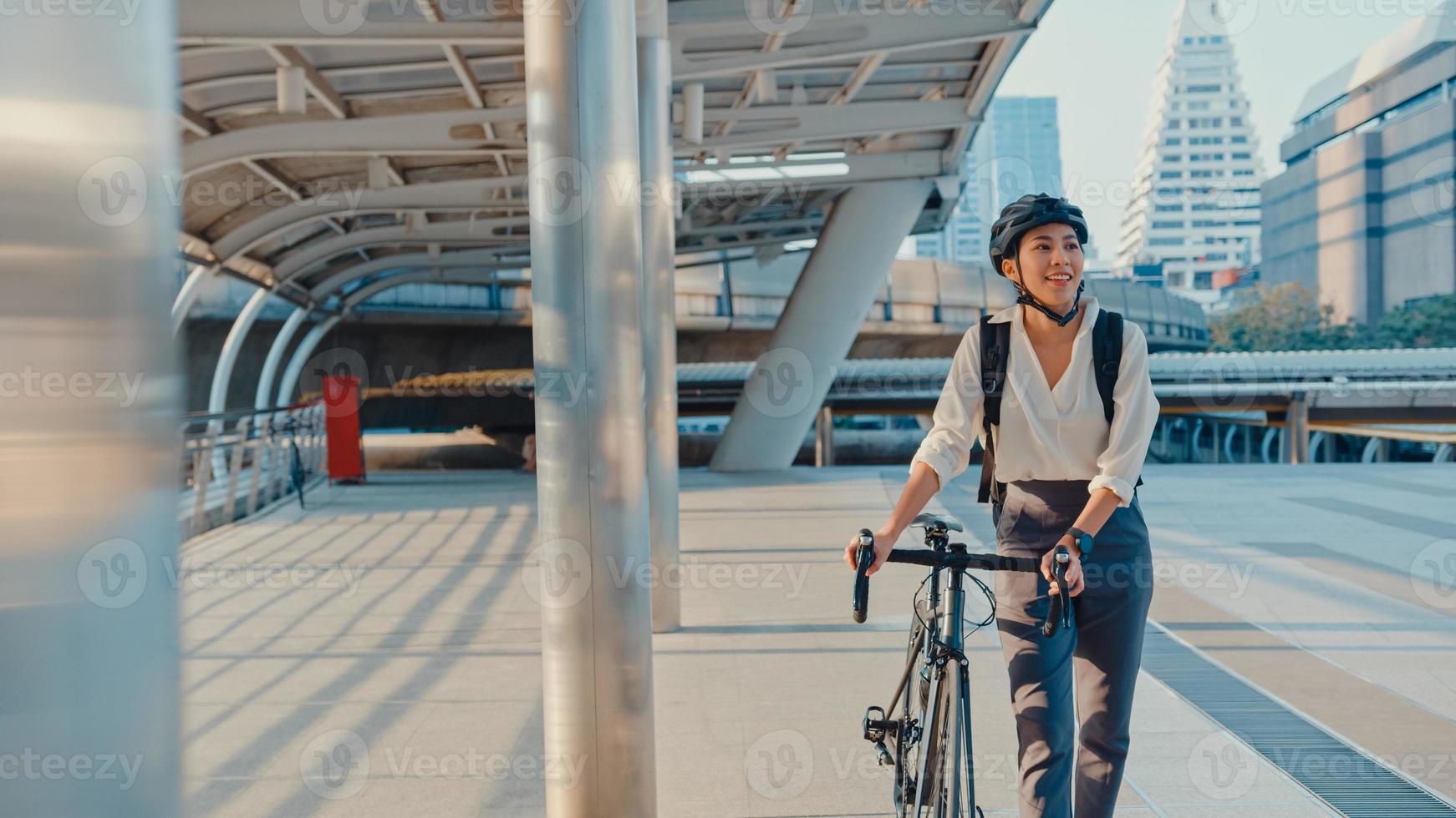 empresária asiática ir trabalhar no escritório andar e sorrir usar mochila olhar ao redor levar bicicleta na rua ao redor do prédio em uma rua da cidade. bicicleta pendulares, comutar de bicicleta, conceito de viajante de negócios. foto