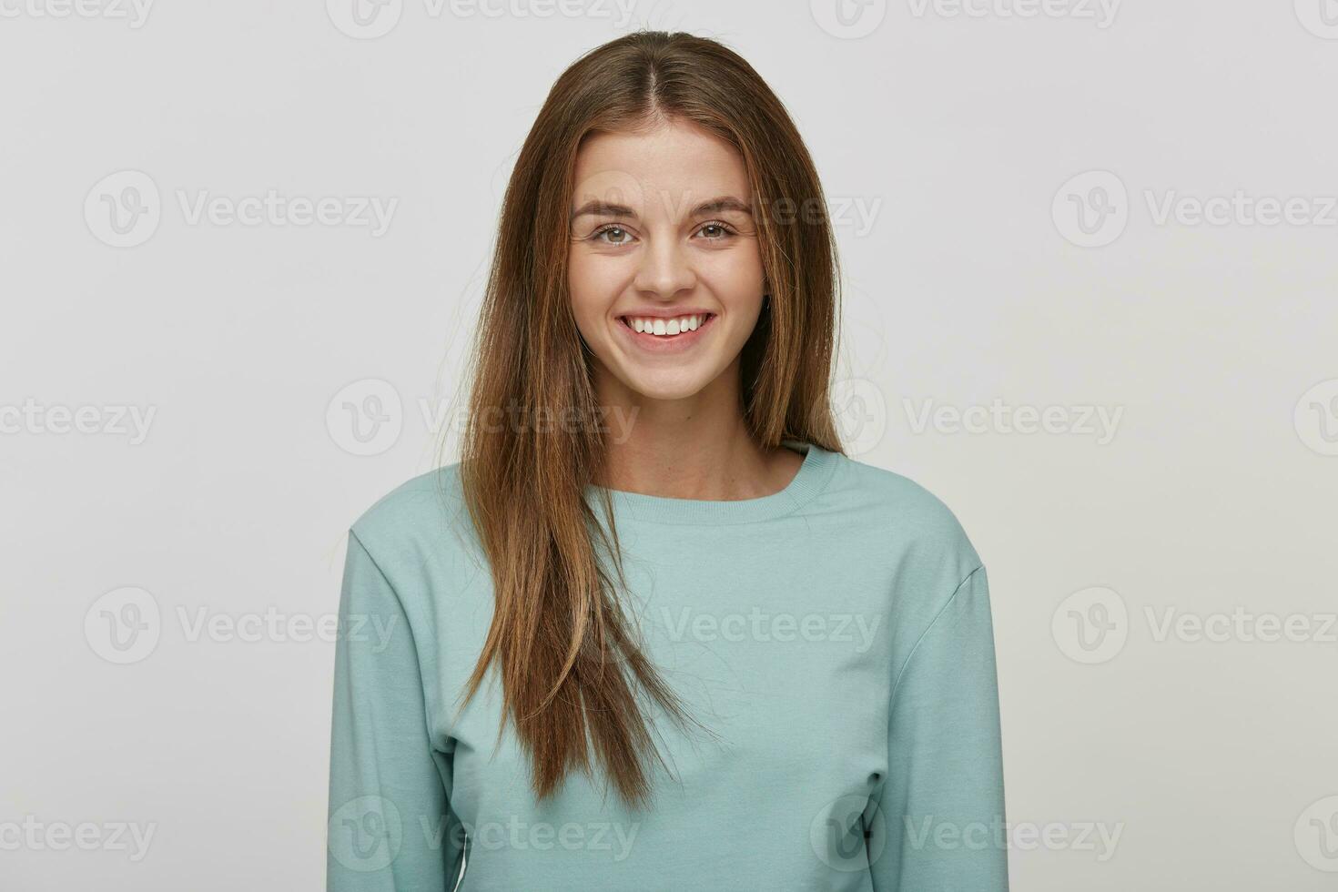 retrato do uma lindo alegre feliz jovem menina com natural Maquiagem e bem cuidado cabelo, sorrisos, desgasta casual azul grandes manga camiseta, em uma branco fundo dentro a estúdio. foto