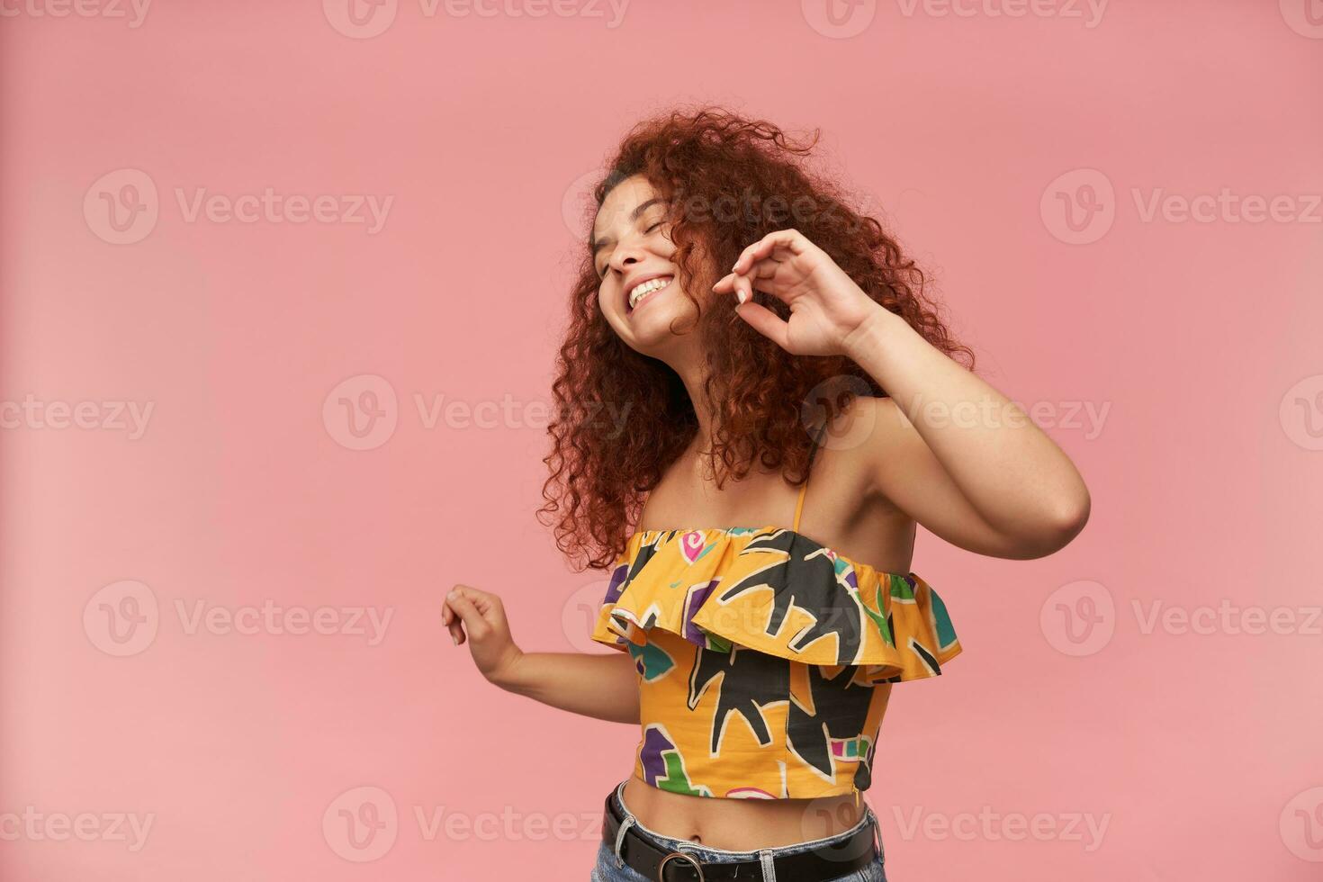 Adolescência garota, feliz olhando mulher com gengibre encaracolado cabelo. vestindo colorida ombros caídos blusa. pessoas e emoção conceito. dançando gostar não 1 assistindo. ficar de pé isolado sobre pastel Rosa fundo foto