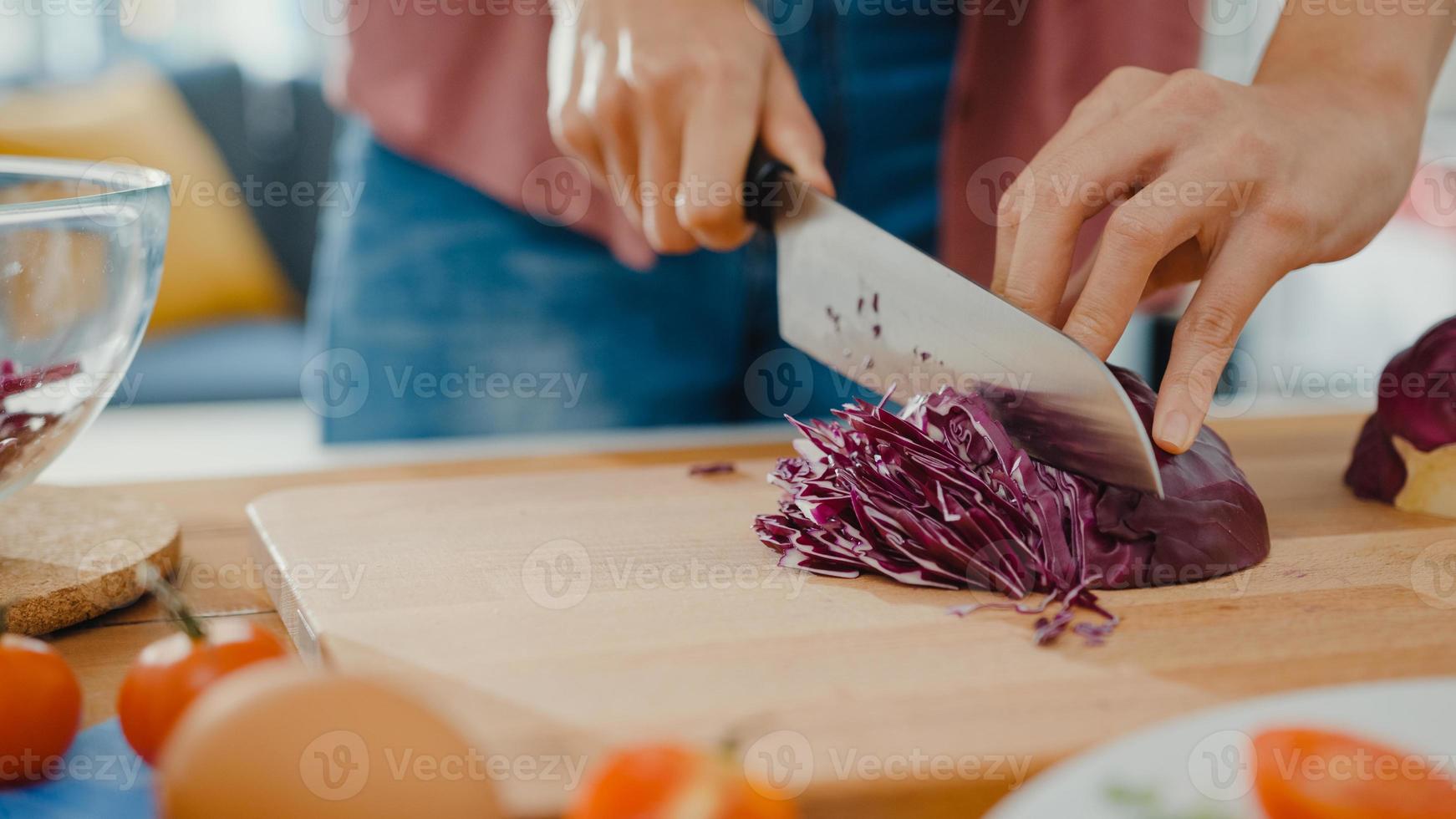 mão do chef jovem mulher asiática segurar faca corte repolho chinês vermelho na placa de madeira na mesa da cozinha em casa. cozinhar salada de legumes, comer alimentos saudáveis de estilo de vida e o conceito natural tradicional. foto