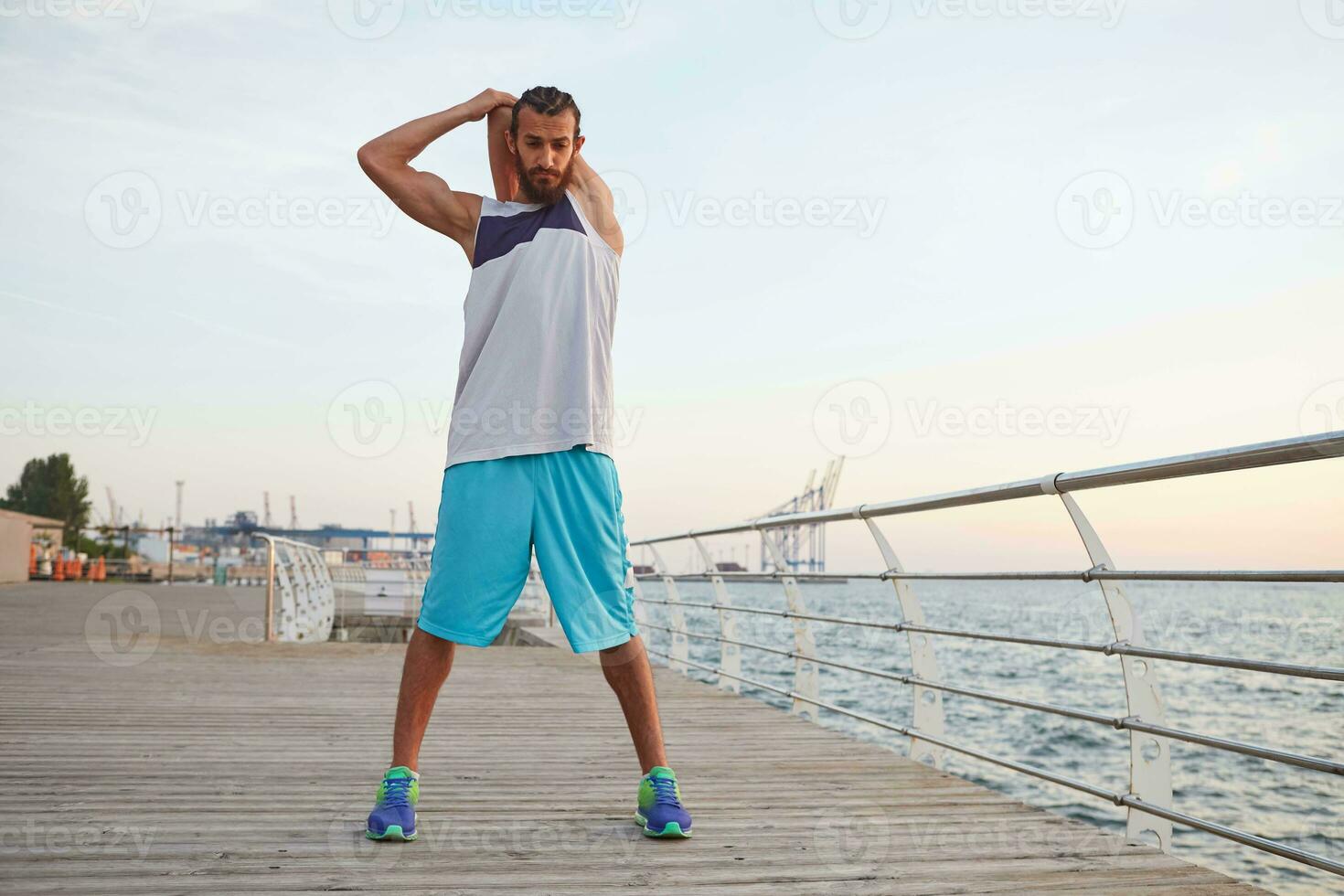 jovem desportivo barbudo cara fazendo uma aquecer depois de uma manhã corre às a à beira-mar, conduz saudável ativo estilo de vida, parece ausente, feios ótimo. foto