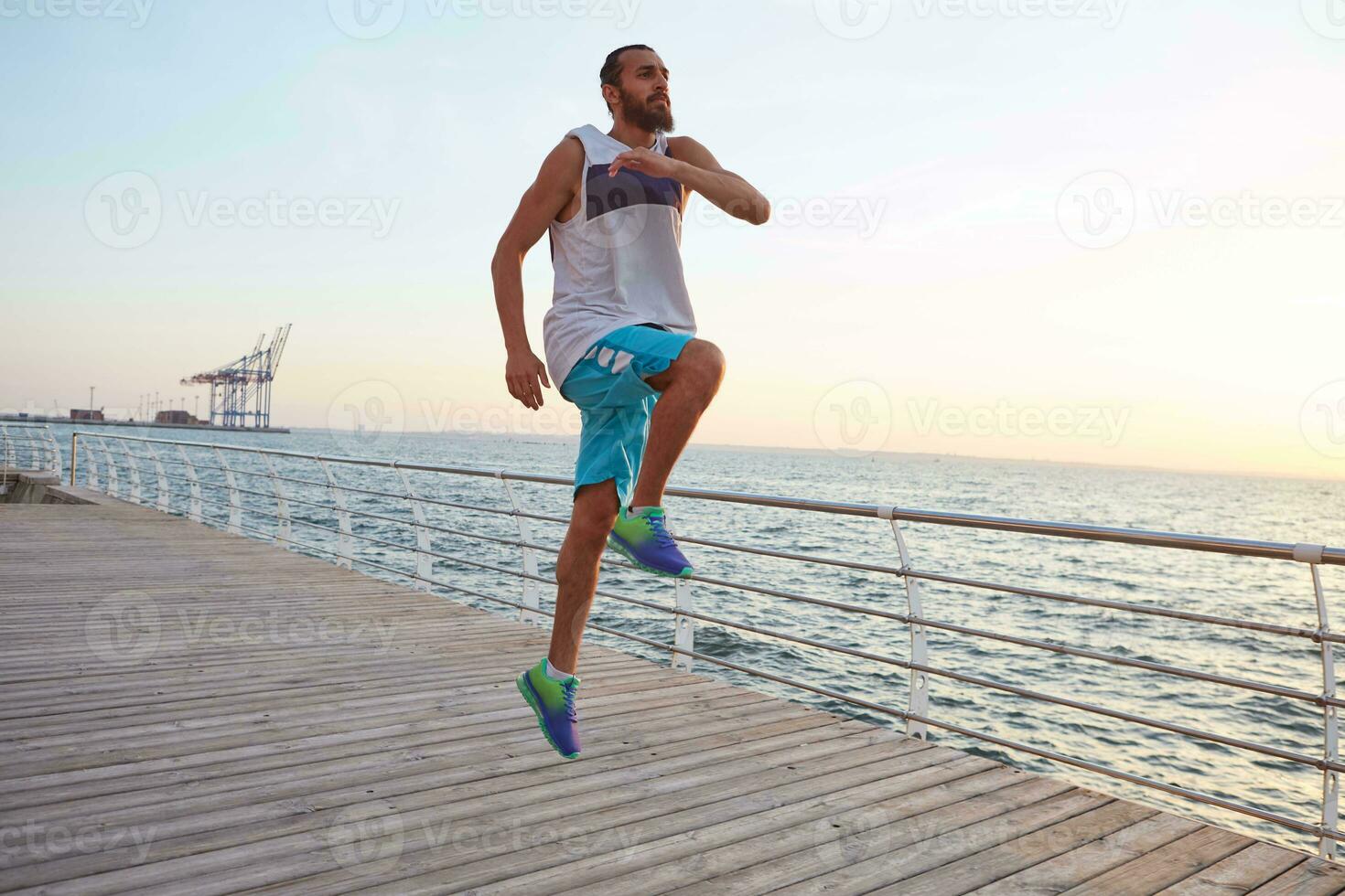 jovem desportivo bonito barbudo pulando cara fazendo manhã exercícios de a mar, aquecer antes correr, conduz saudável ativo estilo de vida. ginástica e esporte conceito. foto