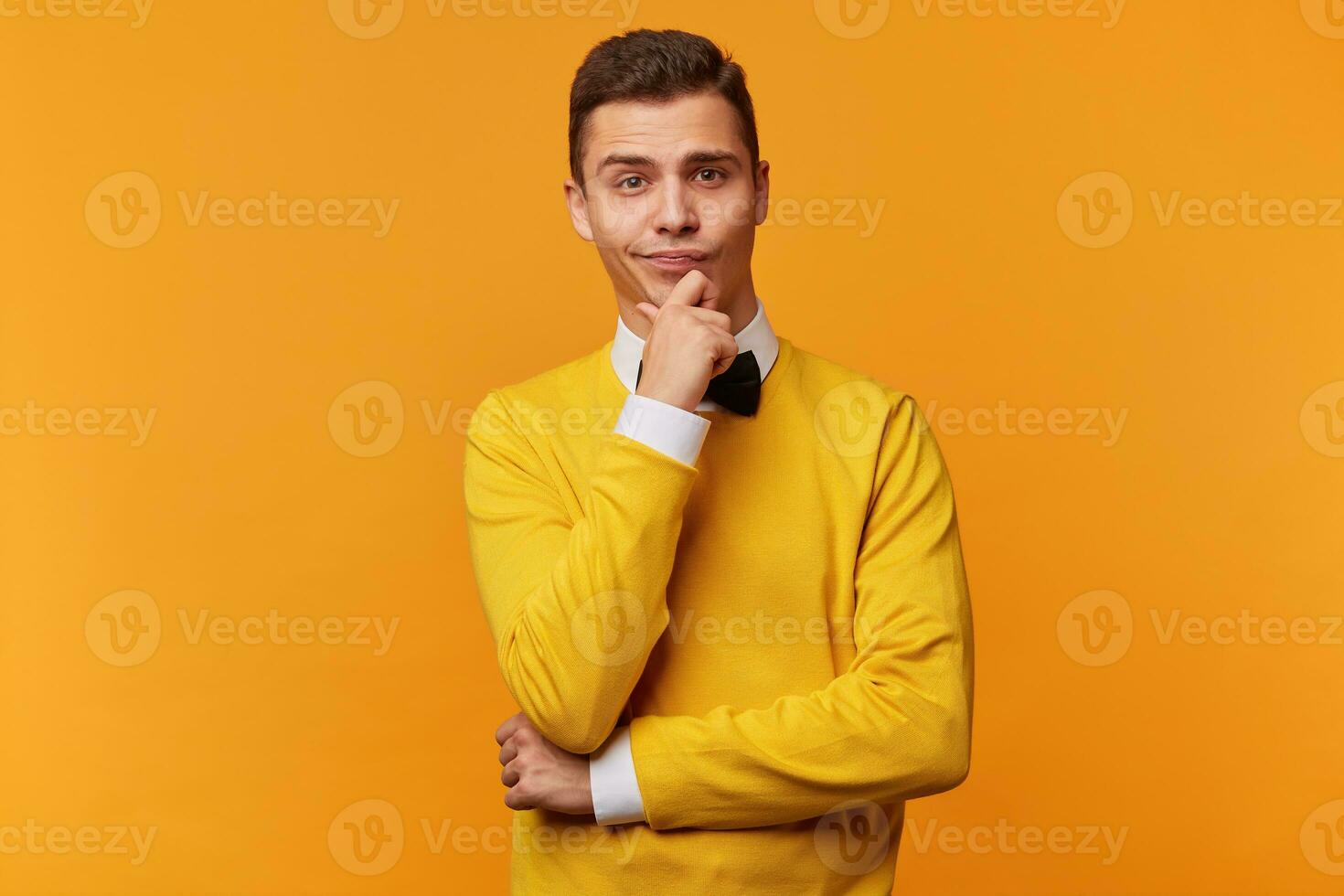 jovem homem focado olhos mantém punho perto a queixo tentando para lembrar algo, profundamente análise a situação, imerso, dentro pensamentos, vestido espertamente, isolado sobre amarelo fundo foto