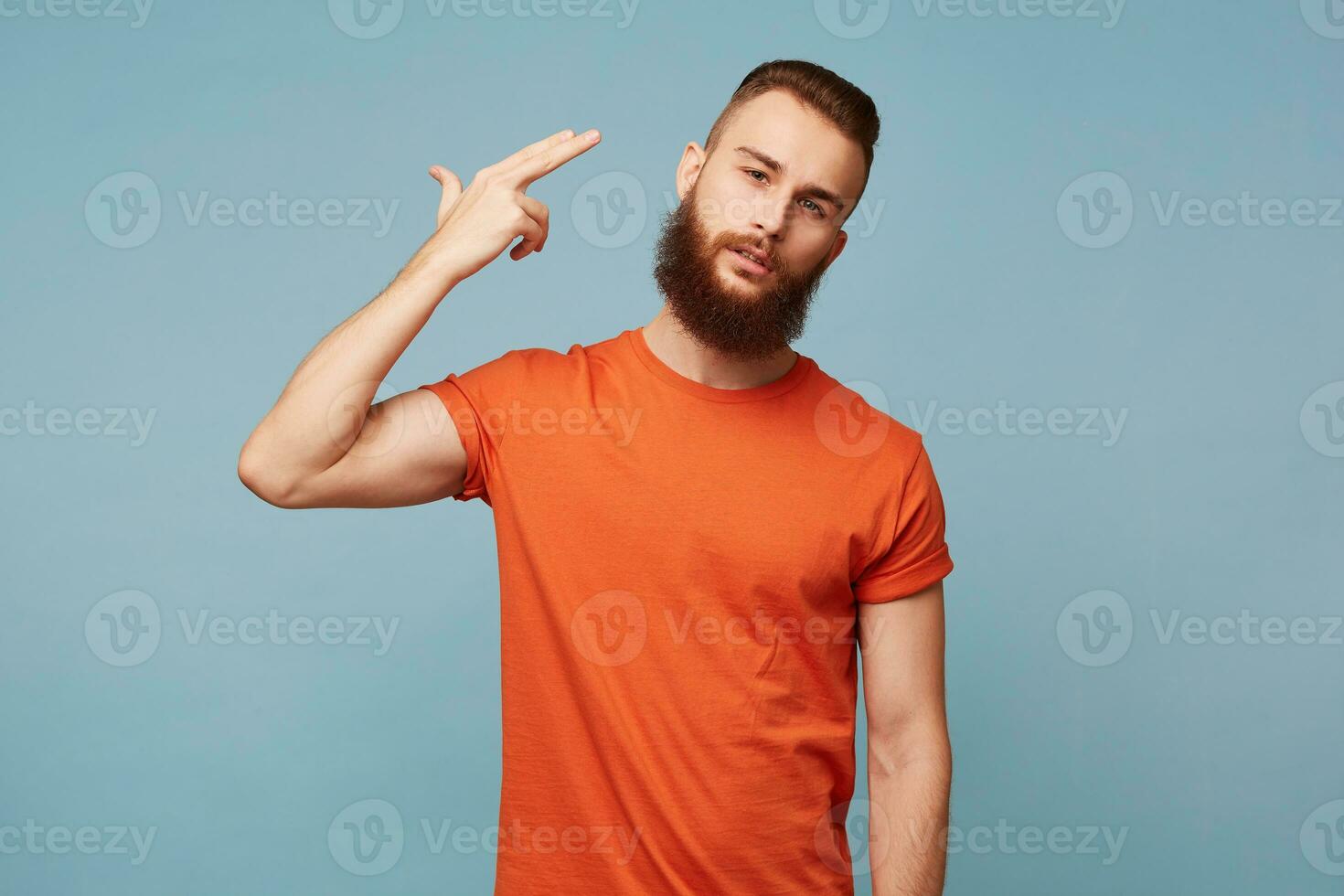 retrato do jovem barbudo homem comprometendo suicídio com dedo arma de fogo gesto. retrato do desesperado cara tiroteio ele mesmo fazer dedo pistola placa contra azul parede fundo. humano face expressões foto