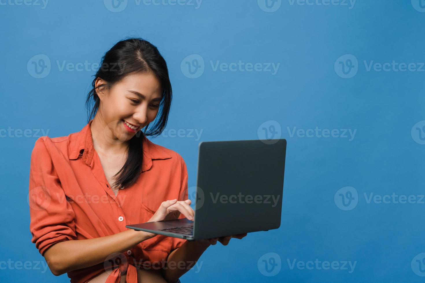 jovem asiática usando laptop com expressão positiva, sorri amplamente, vestida com roupas casuais, sentindo felicidade e carrinho isolado sobre fundo azul. feliz adorável feliz mulher alegra sucesso. foto