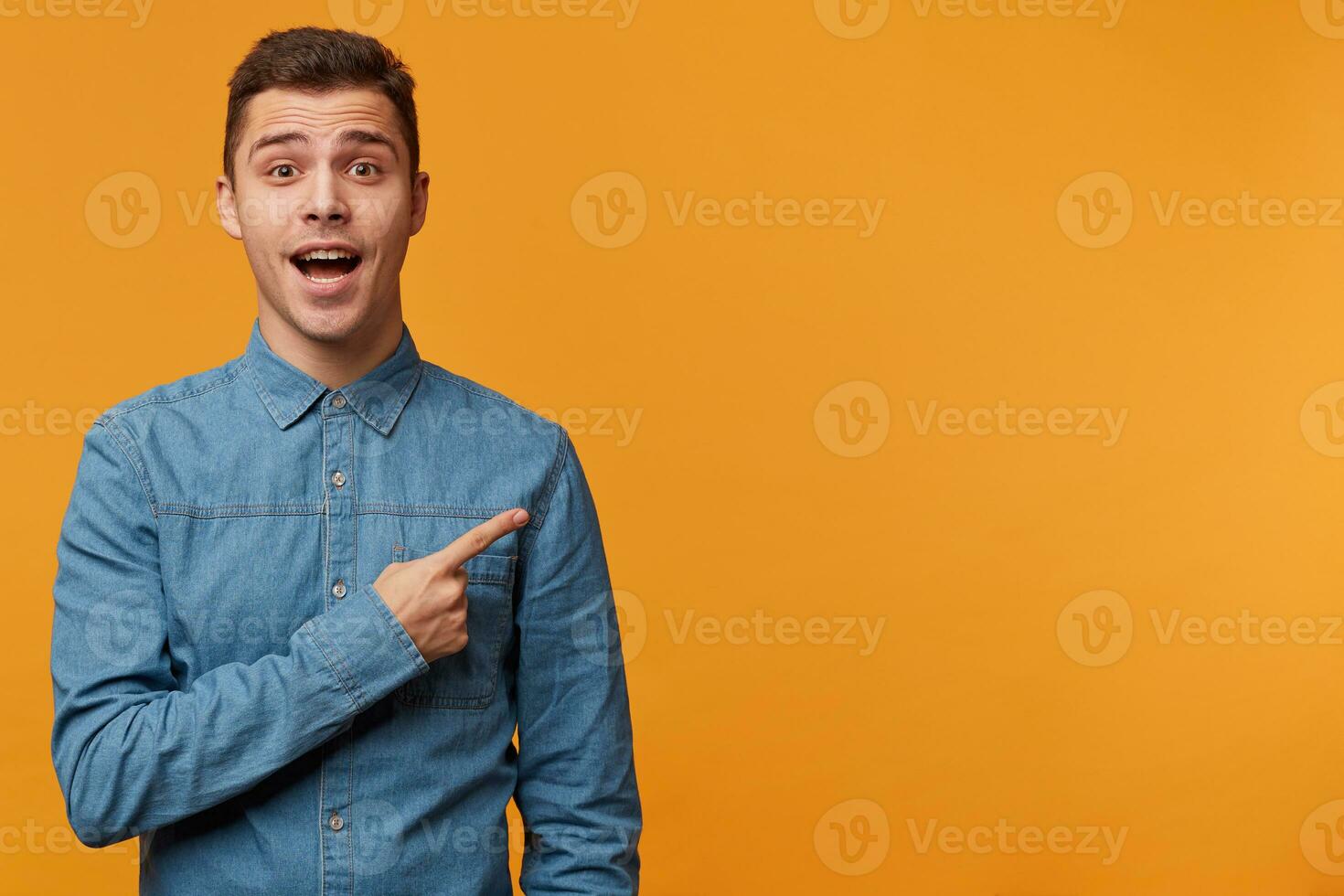 a inspirado jovem homem dentro uma jeans camisa pergunta para pagar atenção para alguma coisa muito interessante importante Novo incrível, apontando com índice dedo para cópia de espaço para seu propaganda ou promoção. foto