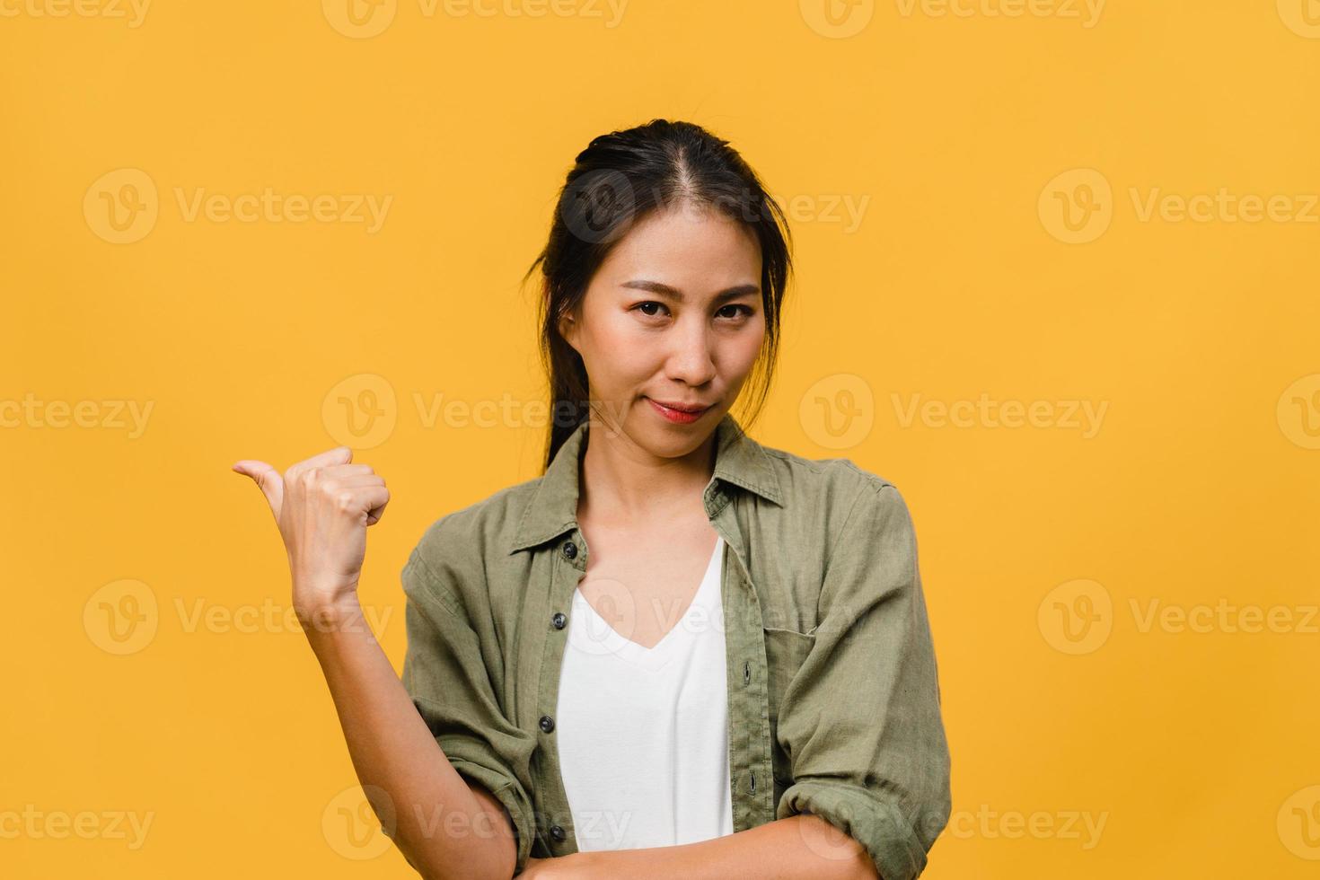 retrato de uma jovem asiática sorrindo com uma expressão alegre, mostra algo incrível no espaço em branco em um pano casual e olhando para a câmera isolada sobre fundo amarelo. conceito de expressão facial. foto