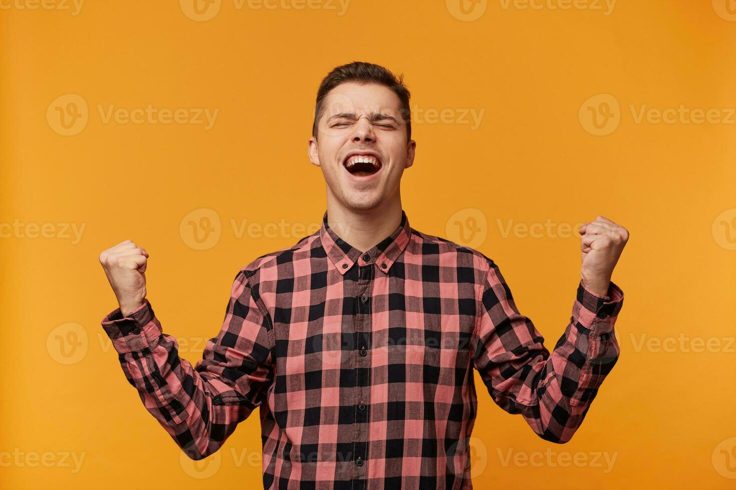 horizontal retrato do uma alegre feliz Loiras homem dentro demim camisa aperto punhos gostar vencedora com olhos fechadas dentro prazer, isolado sobre amarelo fundo foto