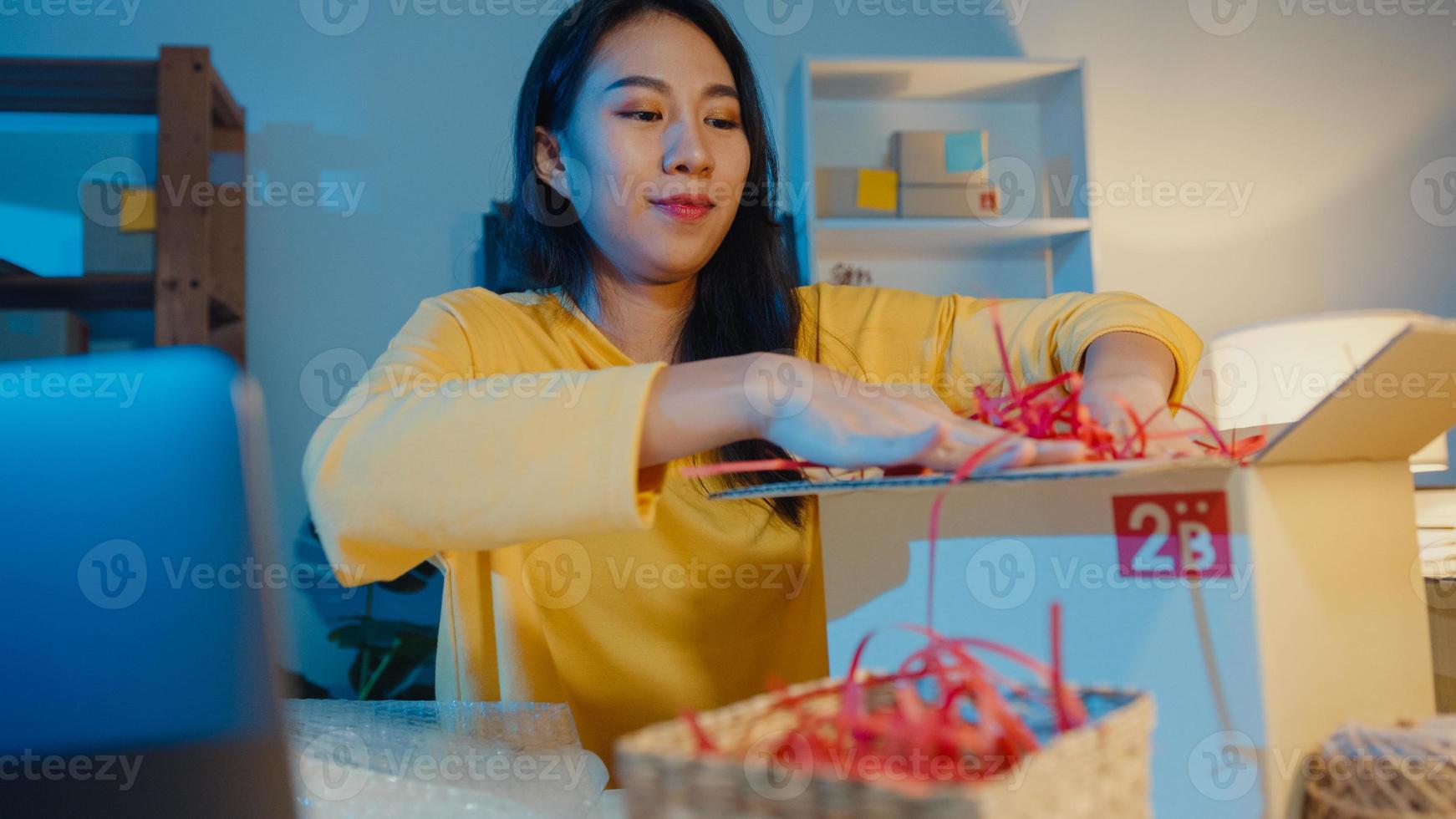 jovem ásia mulher embalagem caixa pacote usar papel para suporte produto fácil dano produto frágil no escritório em casa à noite. proprietário de uma pequena empresa, entrega de mercado online, conceito freelance de estilo de vida. foto