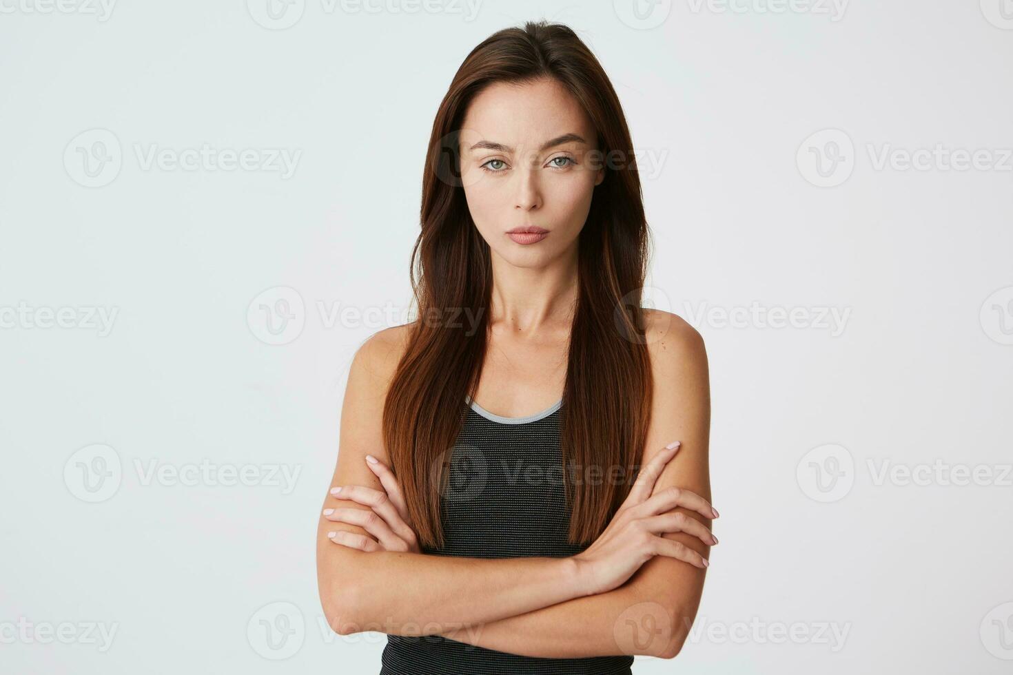 retrato do sério confiante lindo jovem mulher em pé com braços cruzado e parece diretamente dentro Câmera isolado sobre branco fundo foto