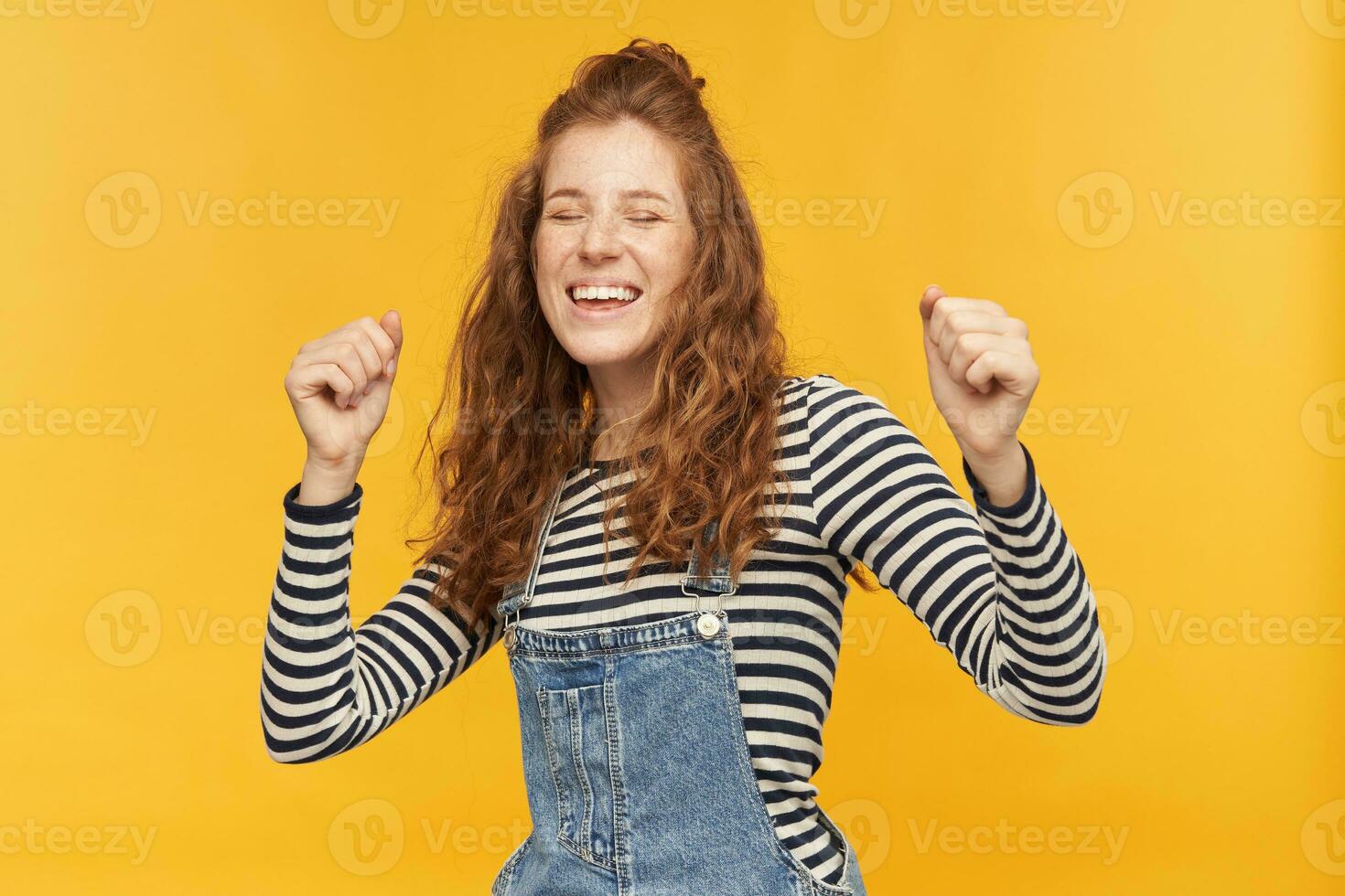interior tiro do alegre engraçado gengibre fêmea, desgasta jeans macacão e despojado camisa, dançando enquanto ouvindo dela favorito música. isolado sobre amarelo fundo. foto