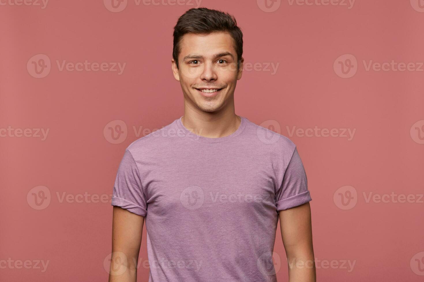 foto do jovem atraente homem dentro blanc camiseta, alegre parece às a Câmera, carrinhos sobre Rosa fundo e sorri.