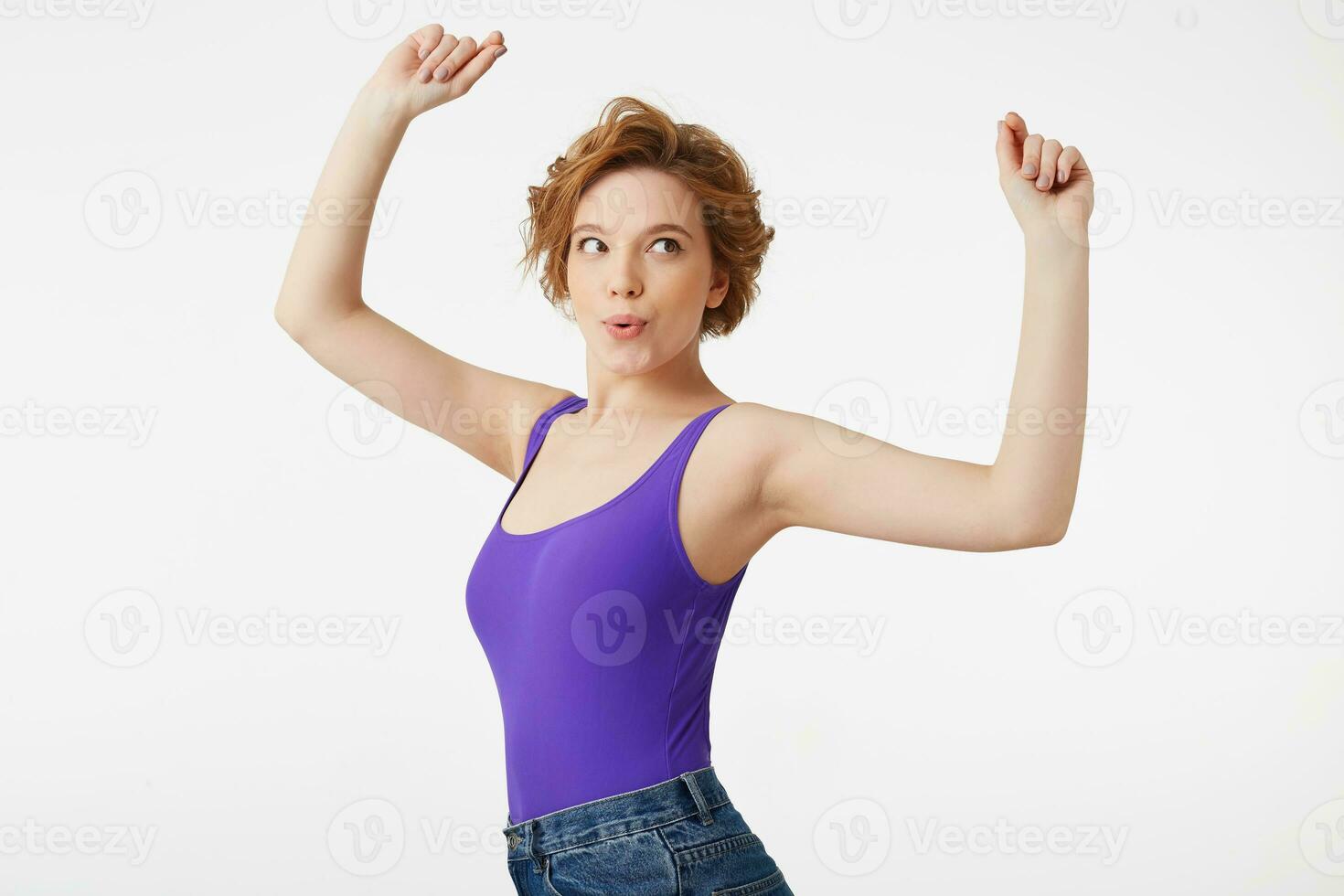 jovem atraente cabelo curto garota, vestindo uma roxa camisa, dançando com dela braços acima desfrutando dela passatempo, fala lábios Uau isolado sobre branco fundo. foto