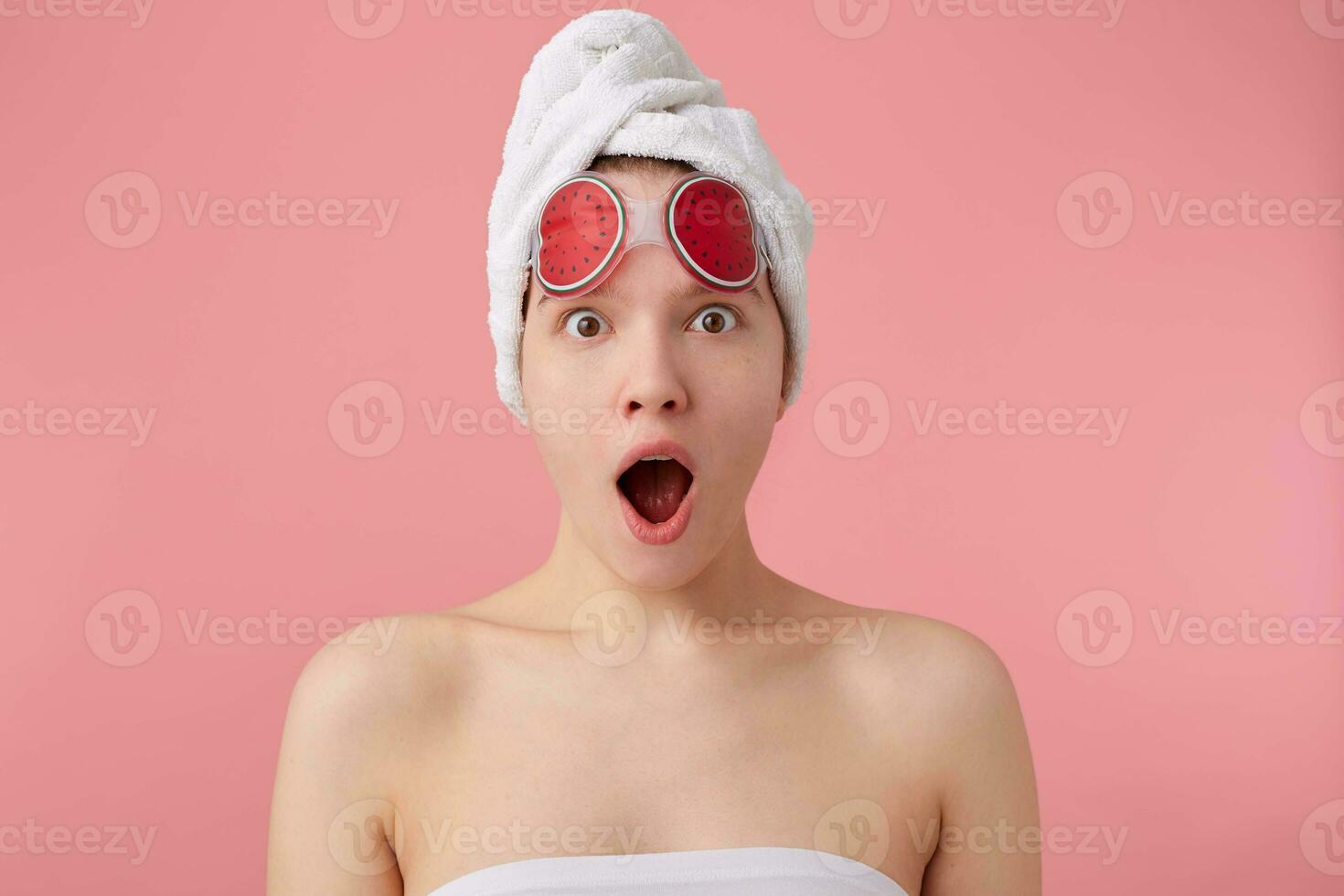 Uau inacreditável notícia jovem espantado menina depois de spa com uma toalha em dela cabeça e mascarar para olhos, com Largo aberto boca e olhos, ouve Novo fofoca, carrinhos sobre Rosa fundo. foto