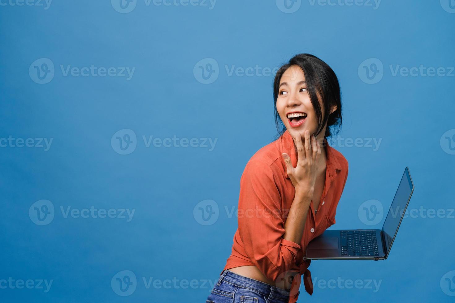 jovem asiática usando laptop com expressão positiva, sorri amplamente, vestida com roupas casuais, sentindo felicidade e carrinho isolado sobre fundo azul. feliz adorável feliz mulher alegra sucesso. foto