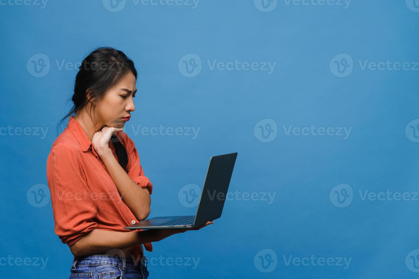 jovem asiática usando laptop com expressão negativa, animado gritando, choro emocional com raiva em um pano casual e ficar isolado sobre um fundo azul com espaço de cópia em branco. conceito de expressão facial. foto