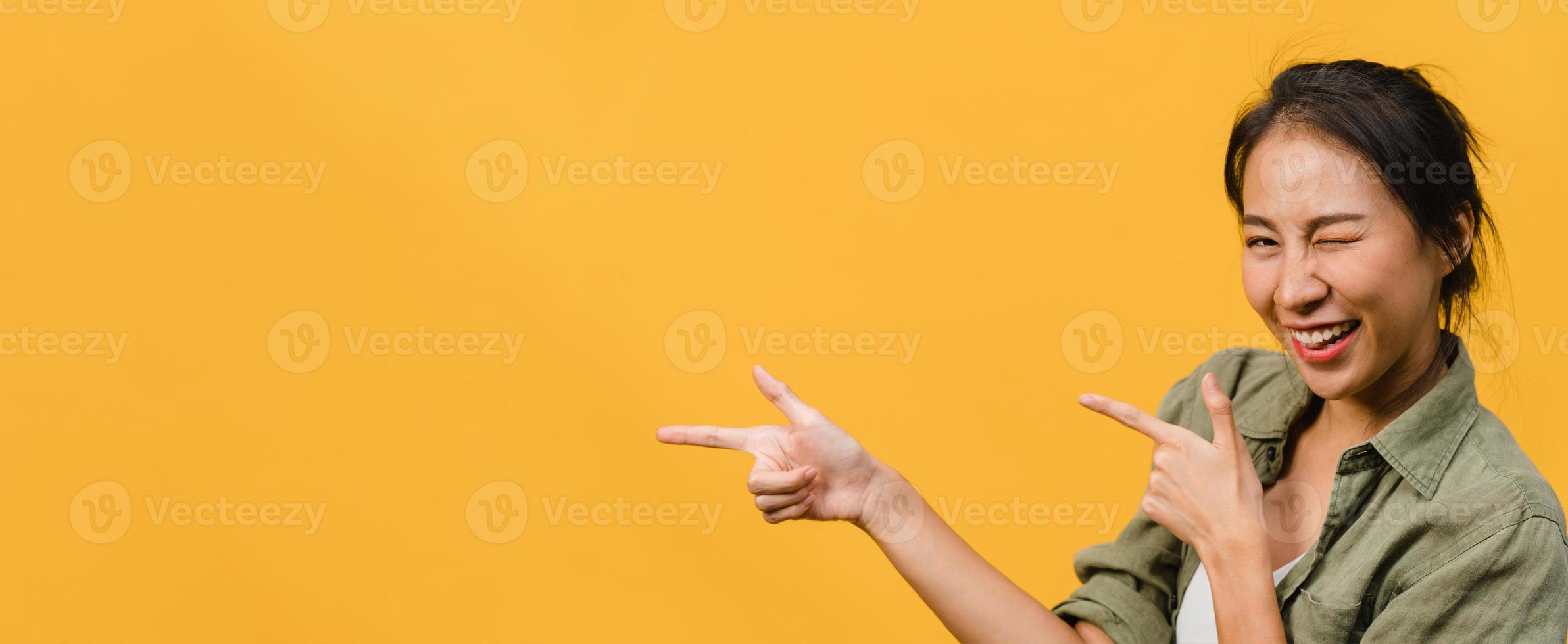 jovem senhora asiática, sorrindo com uma expressão alegre, mostra algo incrível no espaço em branco em um pano casual e olhando para a câmera isolada sobre fundo amarelo. banner panorâmico com espaço de cópia. foto