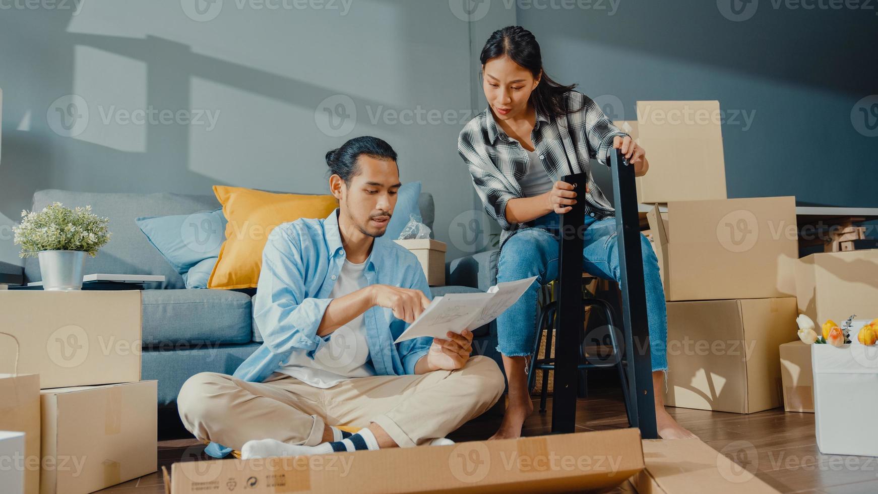 feliz asiático jovem atraente casal homem e mulher ajudam uns aos outros a desempacotar a caixa e montar a mobília, decorar a mesa de construção de casa com caixa de papelão na sala de estar. jovem asiático se casou com o conceito de casa. foto