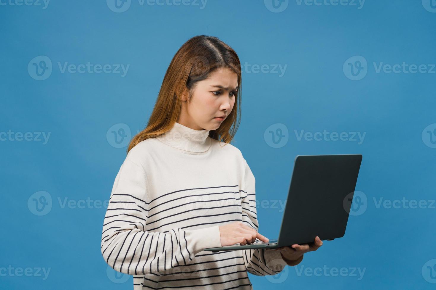 jovem asiática usando laptop com expressão negativa, animado gritando, choro emocional com raiva em um pano casual e ficar isolado sobre um fundo azul com espaço de cópia em branco. conceito de expressão facial. foto