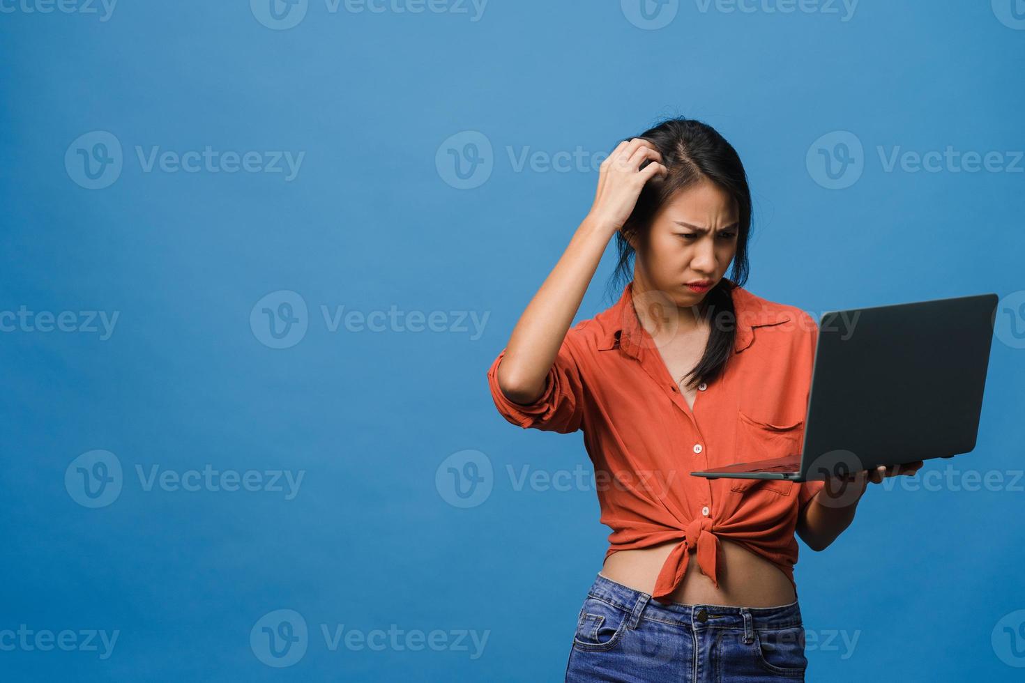 jovem asiática usando laptop com expressão negativa, animado gritando, choro emocional com raiva em um pano casual e ficar isolado sobre um fundo azul com espaço de cópia em branco. conceito de expressão facial. foto