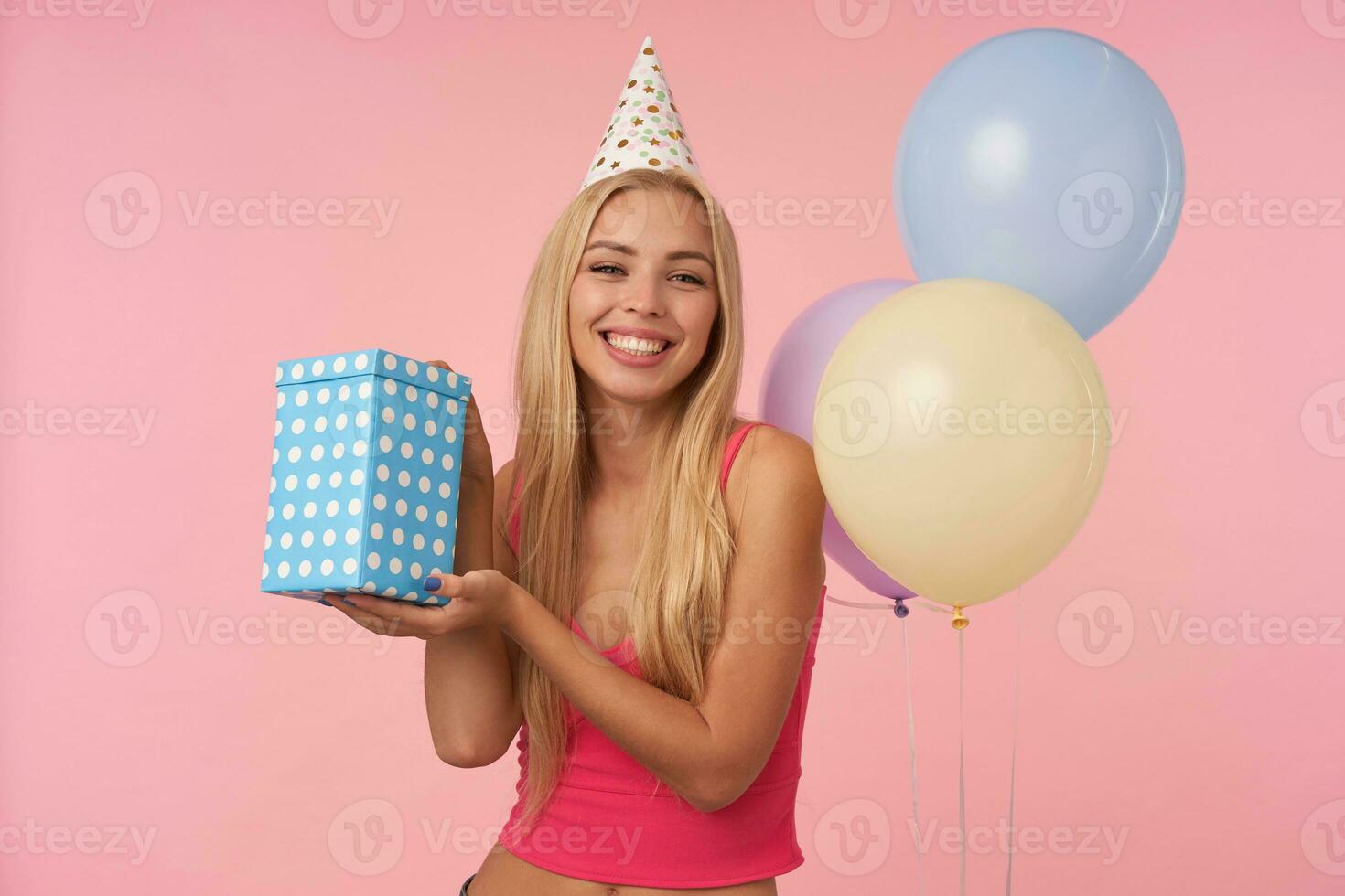 estúdio foto do feliz jovem grandes cabelos Loiras mulher com casual Penteado regozija-se agradável festa juntos com amigos, comemora aniversário, posando sobre Rosa fundo com multicolorido ar balões